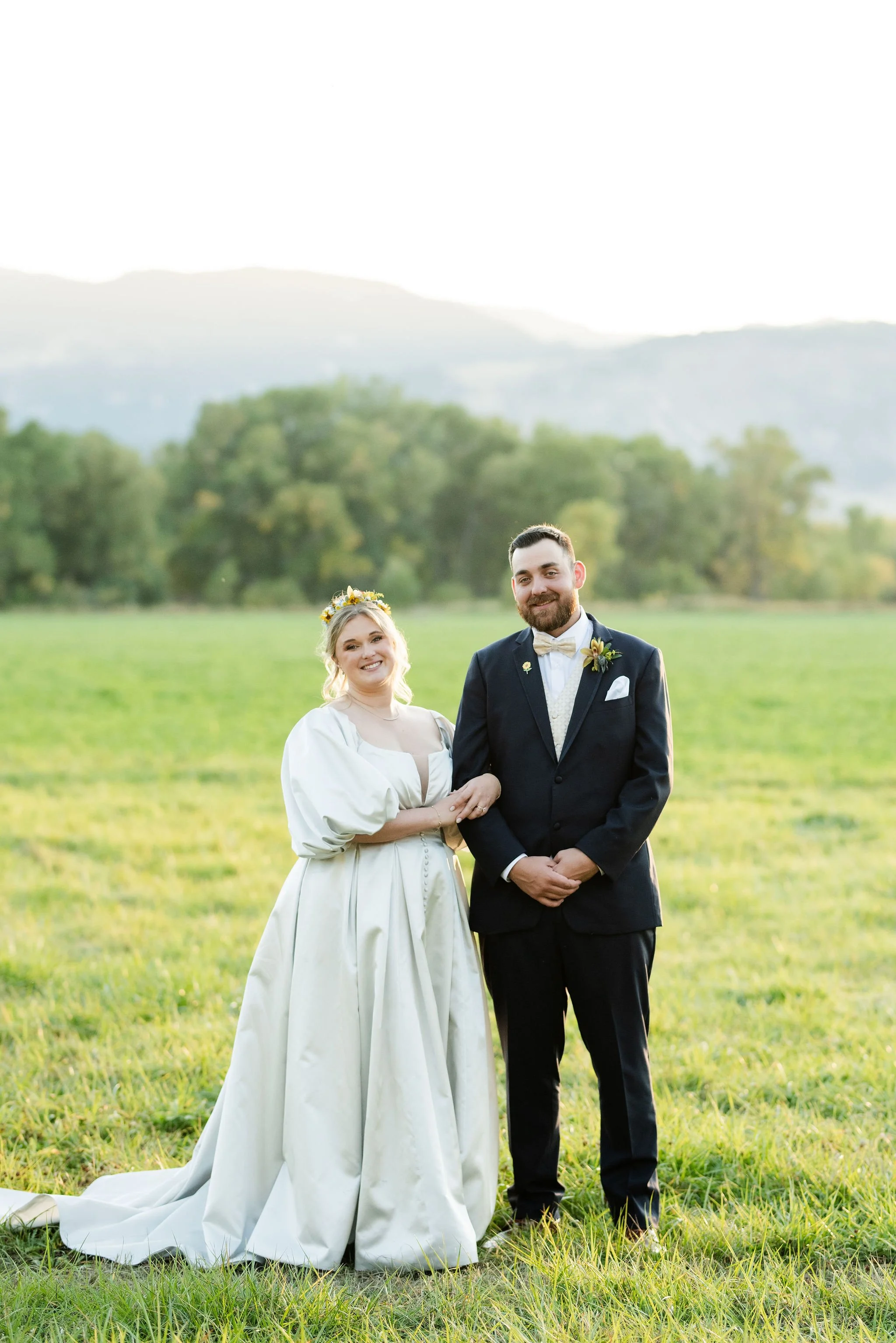 A bride and groom stand in a green field with the Bighorn Mountains in the background following their September wedding in Dayton, WY with flowers by Whirly Girl Flowers, a wedding florist from Sheridan, WY
