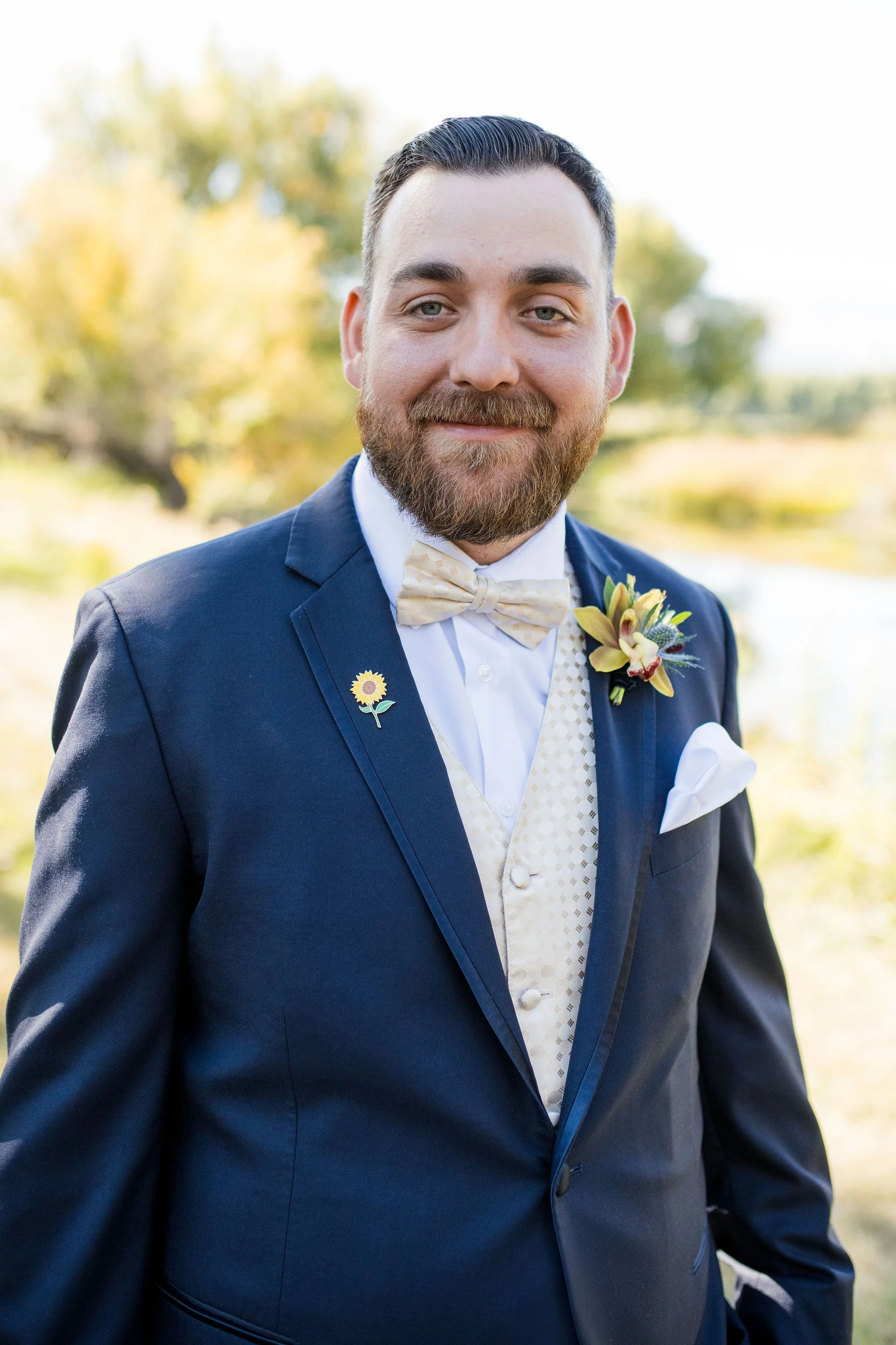 A groom wearing a navy suit with a fall inspired boutonniere in golden tones with a wildflower feel for a September wedding in Dayton, WY with flowers from Sheridan, WY wedding florist Whirly Girl Flowers