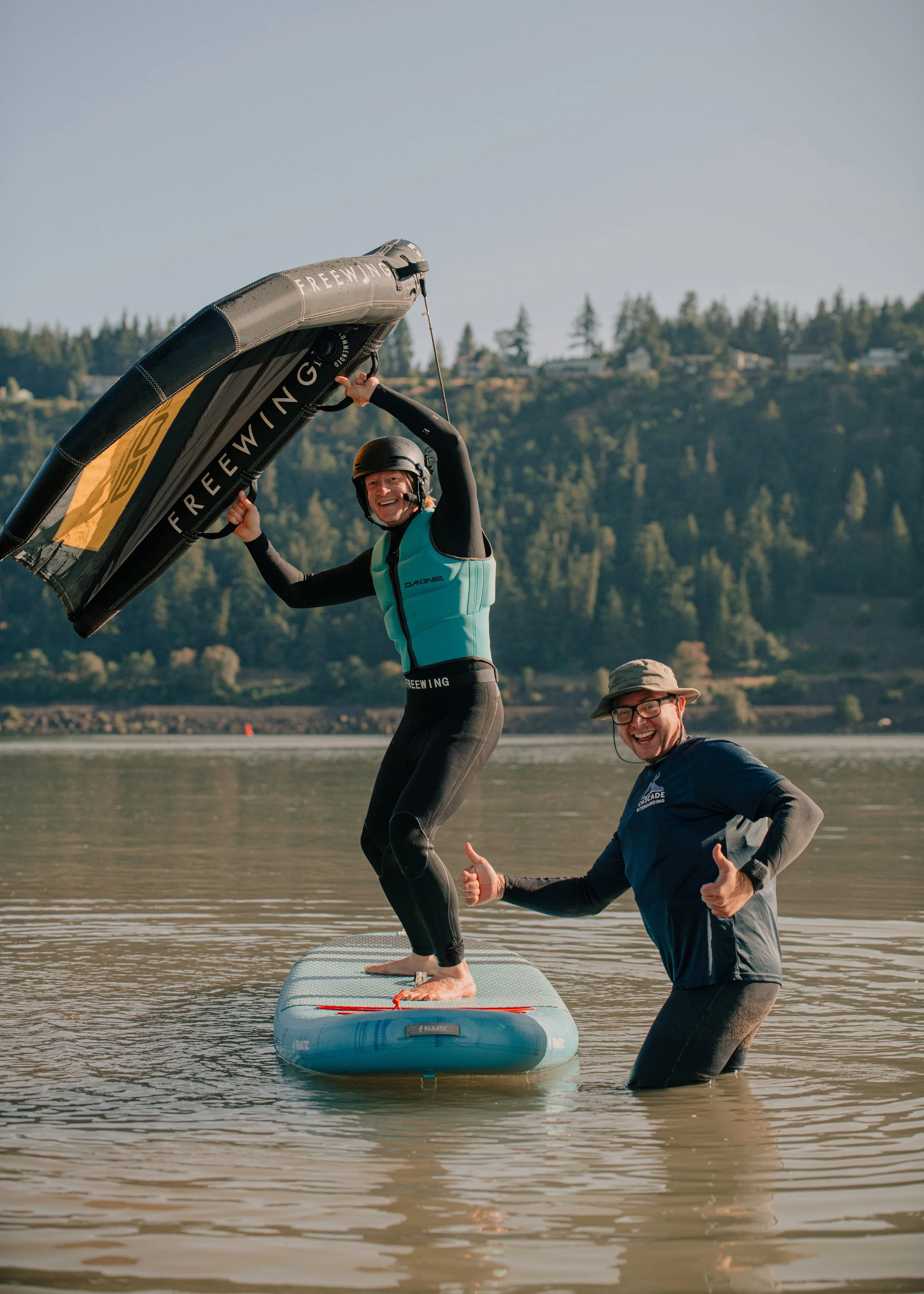 This impage portrays a Cascade Kiteboarding and Winging instructor teaching a student a fundamental wing lesson. Student is standing on a SUP board and flying the wing.