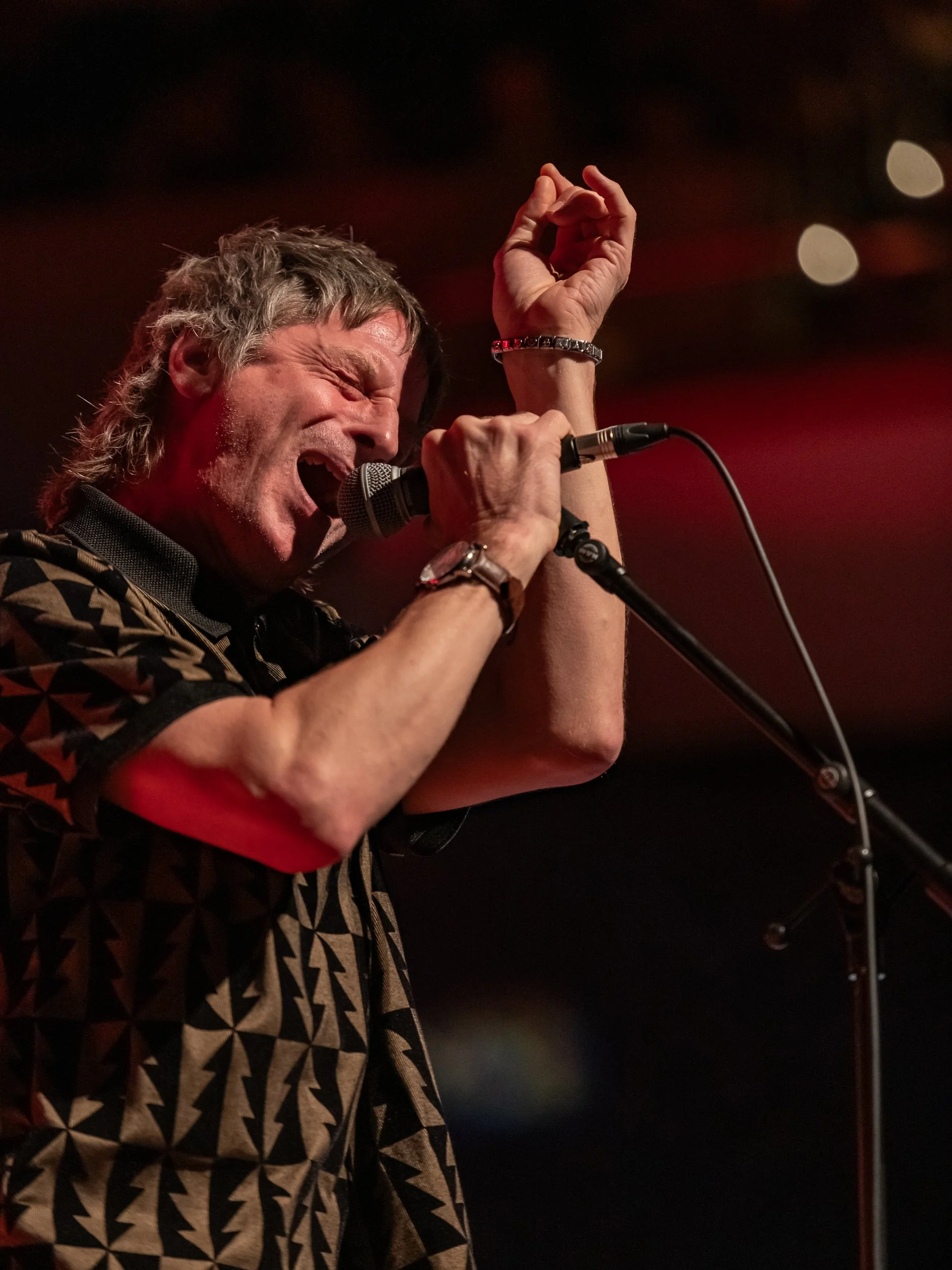 A middle-aged man singing passionately into a microphone during a live performance, with eyes closed and one hand raised.