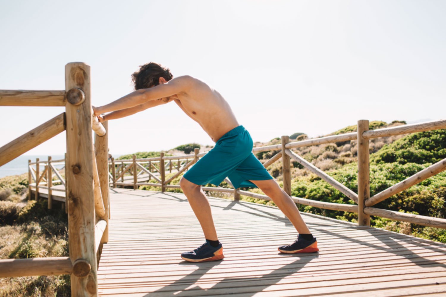 Male runner performing post-run calf stretch on coastal boardwalk as part of recovery protocol and cool-down routine
