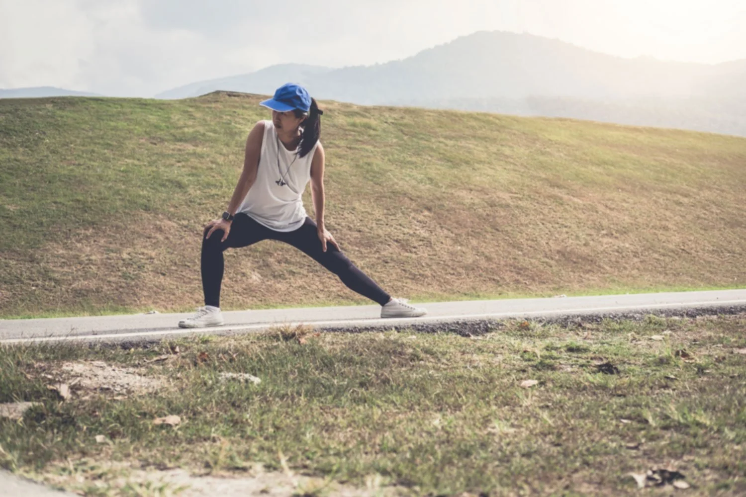 Female athlete performing lateral lunge stretch on mountain road to build hip mobility and single-leg stability for running