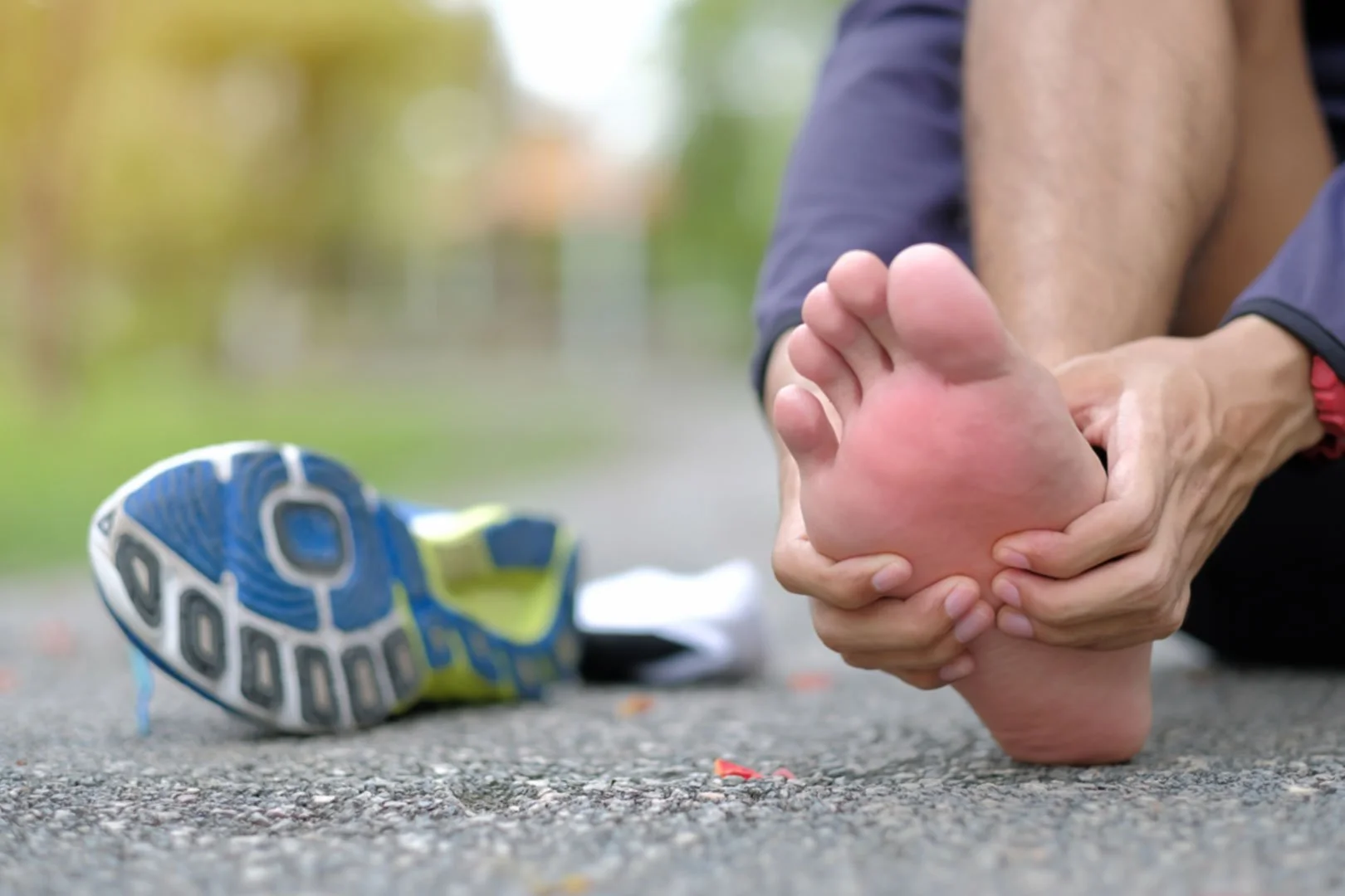 Runner sitting on pavement holding painful heel after long run, shoe removed