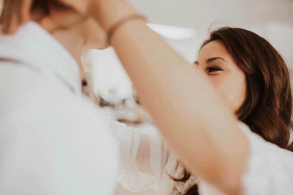 Woman adjusting a man's collar or shirt indoors, close-up.