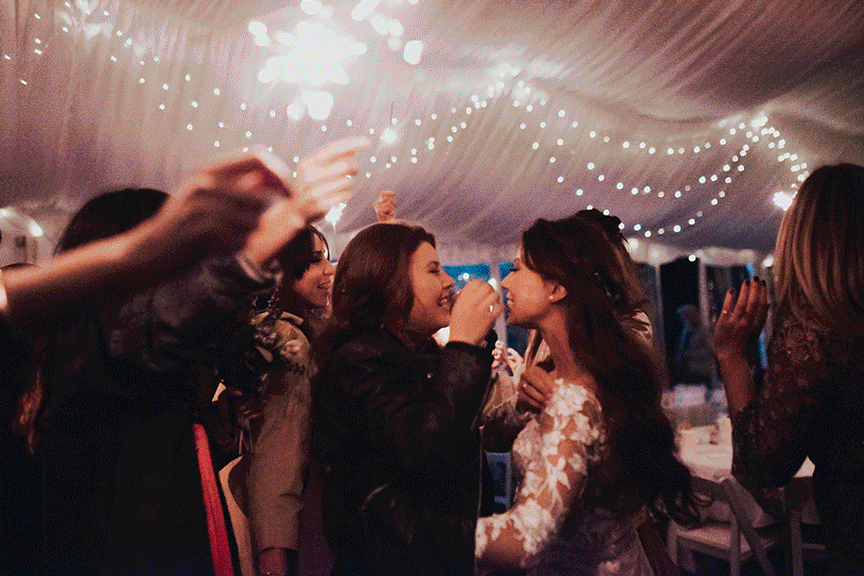 Group of people celebrating with sparklers under string lights in a tent.