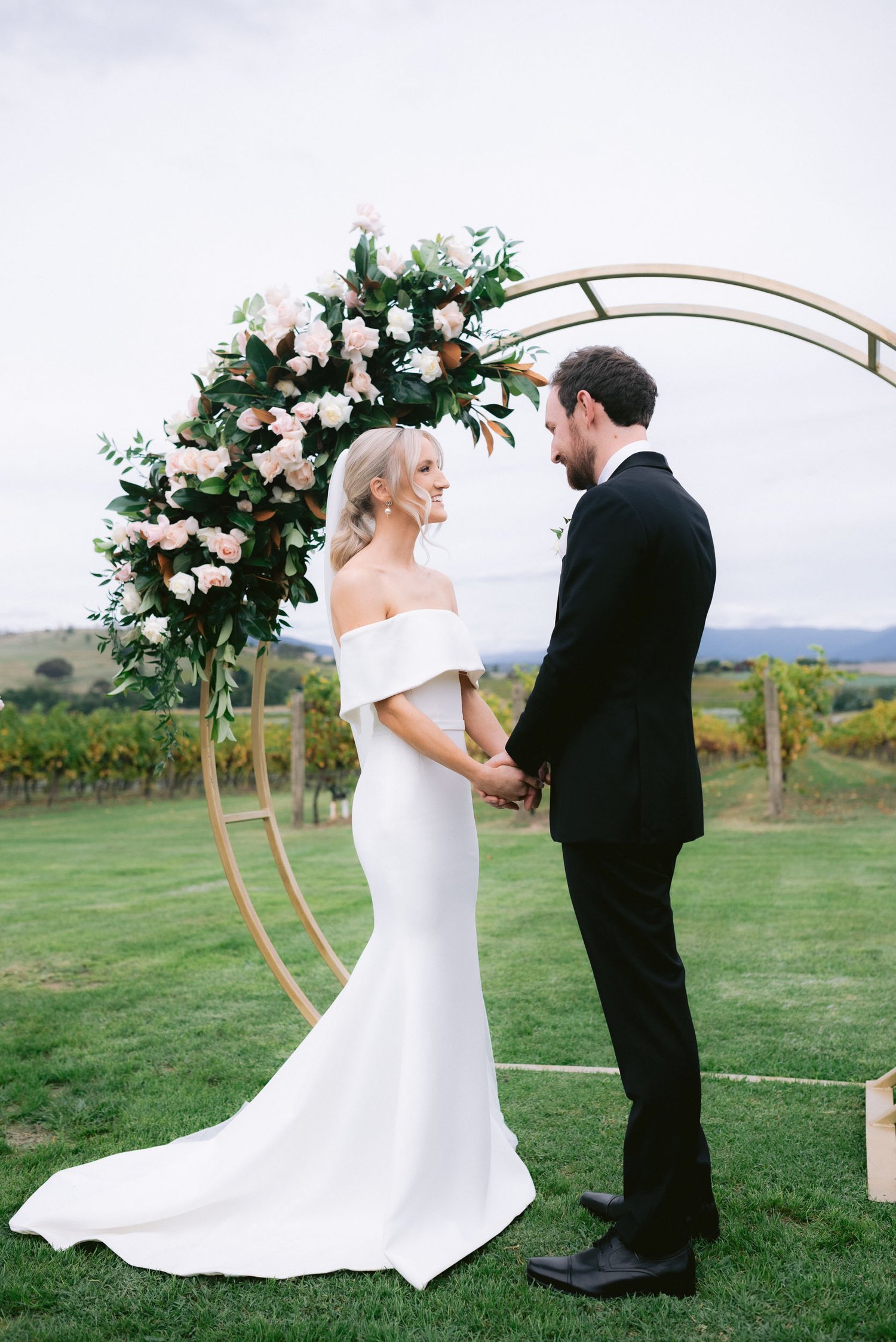 Bride and groom standing under a floral arch during an outdoor wedding ceremony at Acacia Ridge Winery.
