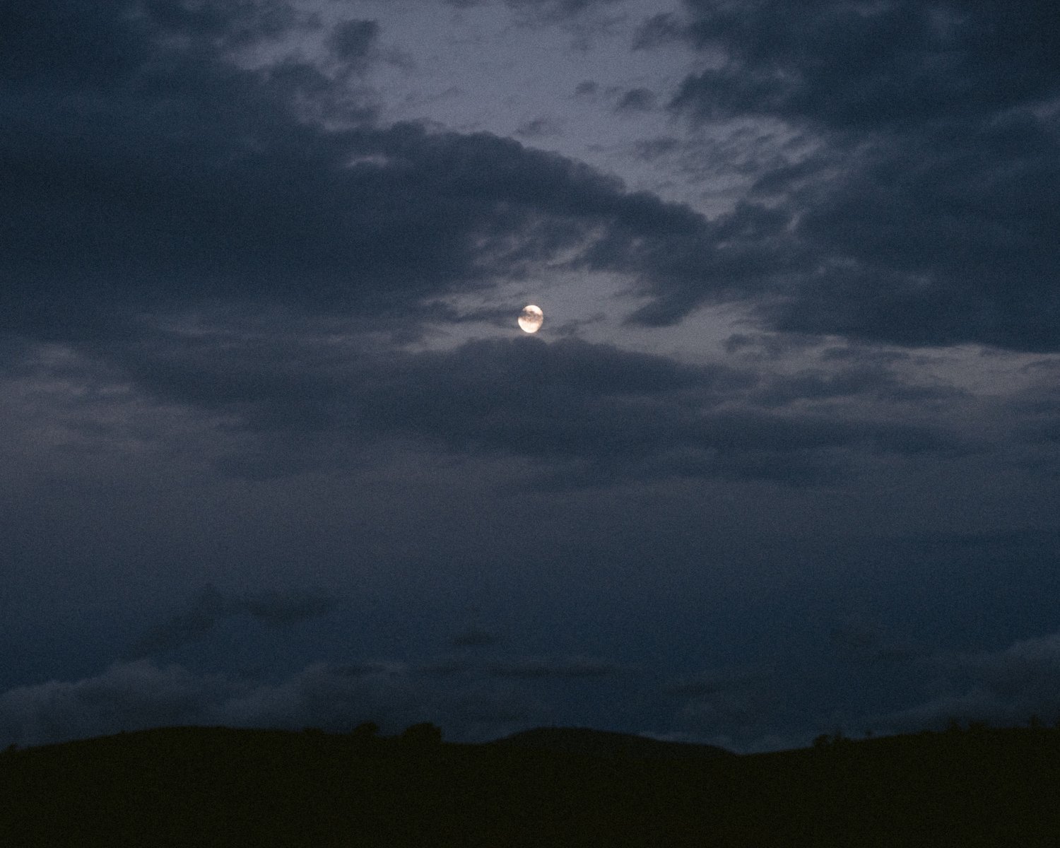 Night sky with a bright moon partially obscured by dark clouds.