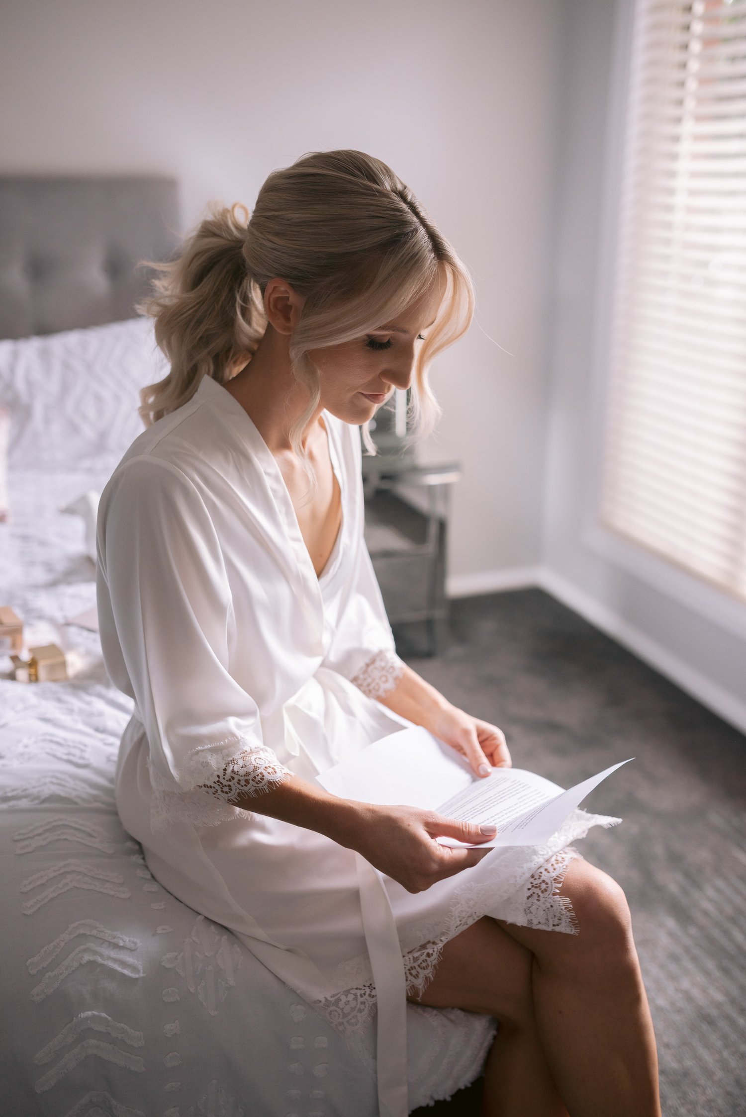 Woman in white robe sitting on a bed reading a letter