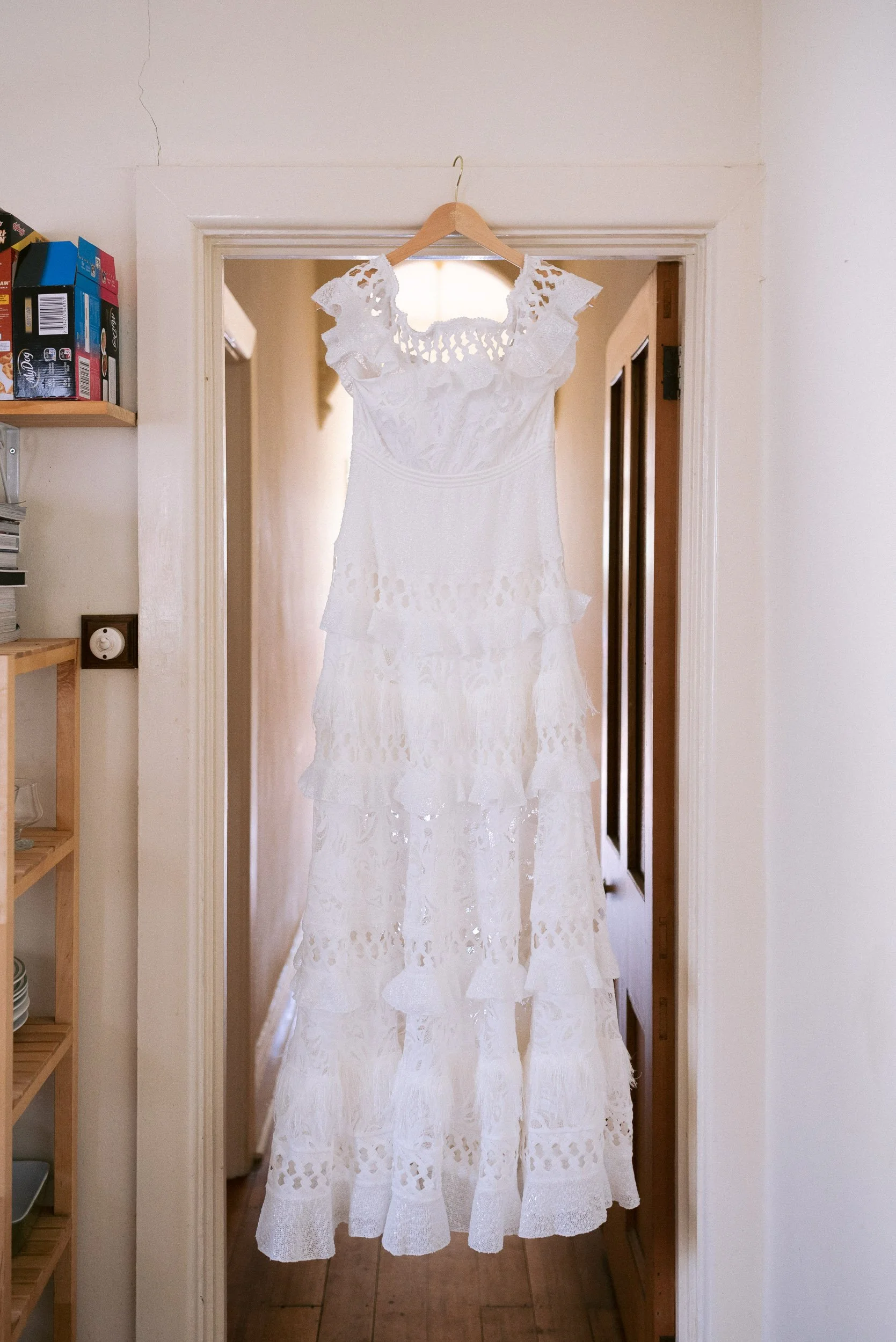 White lace dress hanging on a wooden hanger in a doorframe.