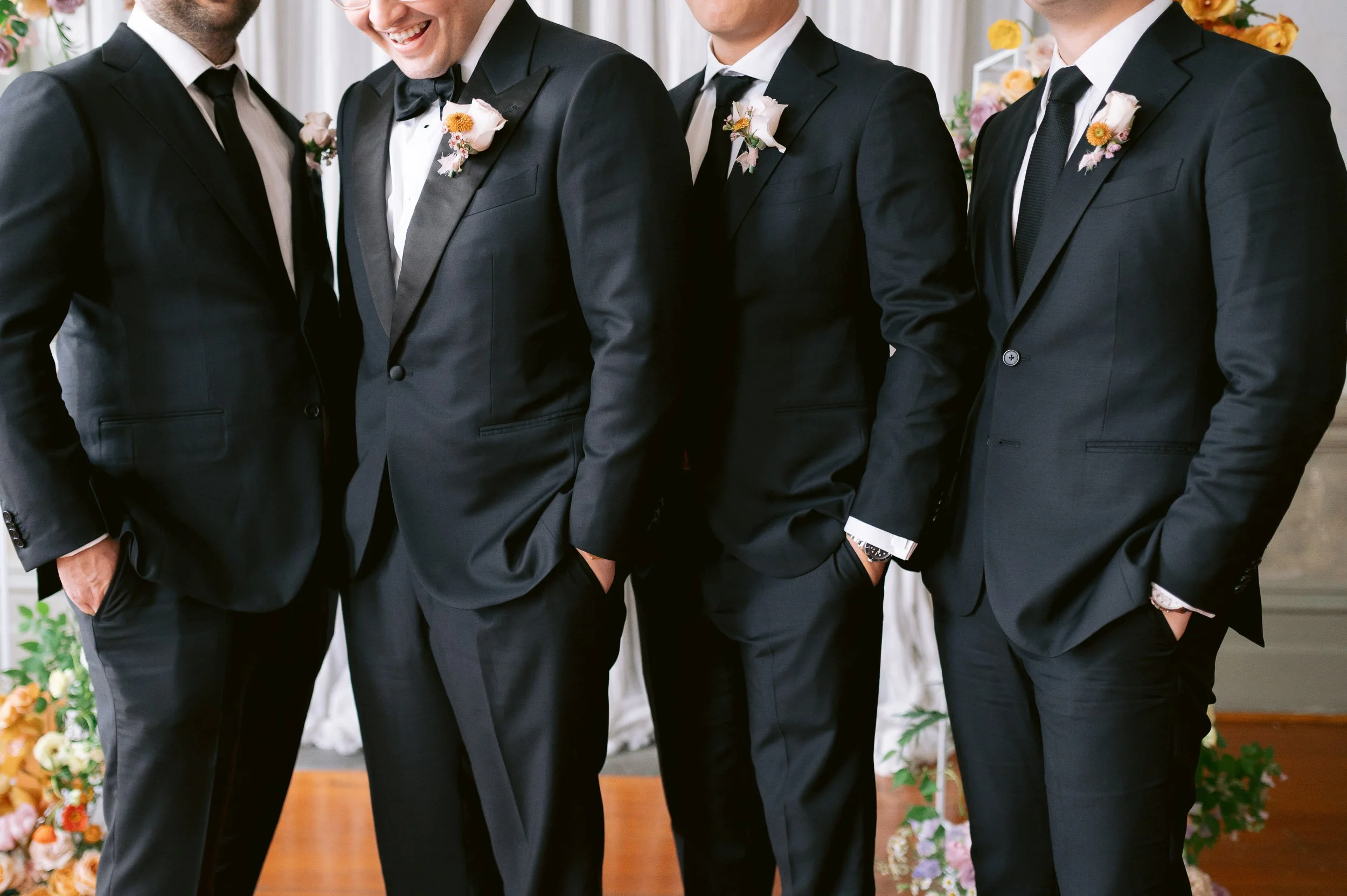 Four men in suits with boutonnieres during a wedding ceremony.