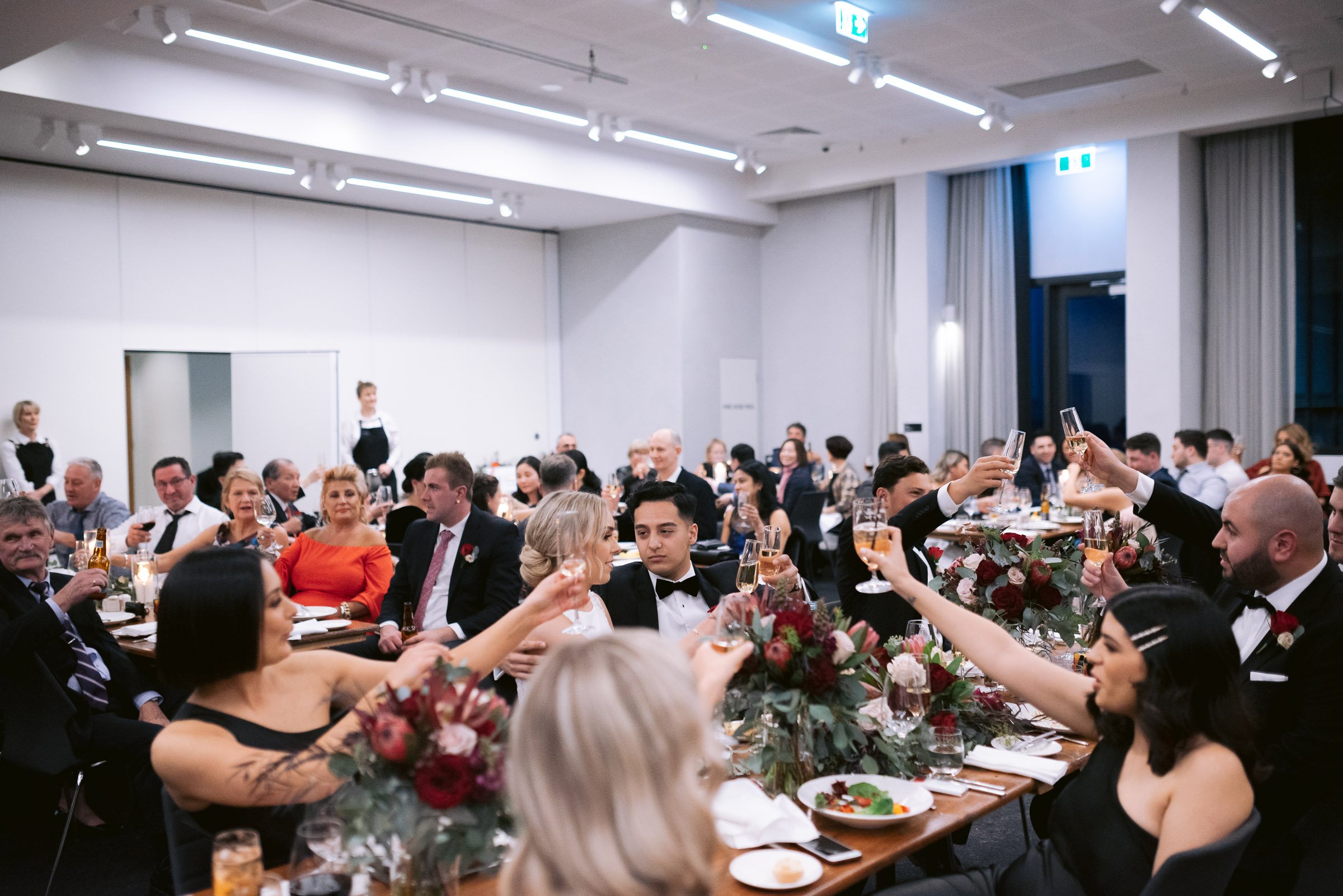 Formal event with seated guests raising glasses in a toast, elegant table settings with floral centerpieces.