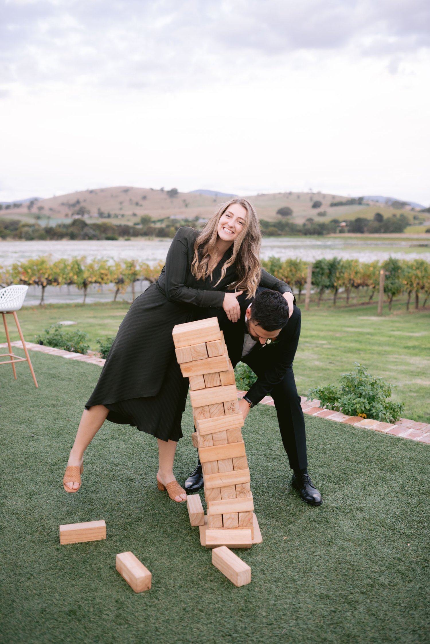 Two people playing giant Jenga outdoors on grass, one smiling as the tower falls.