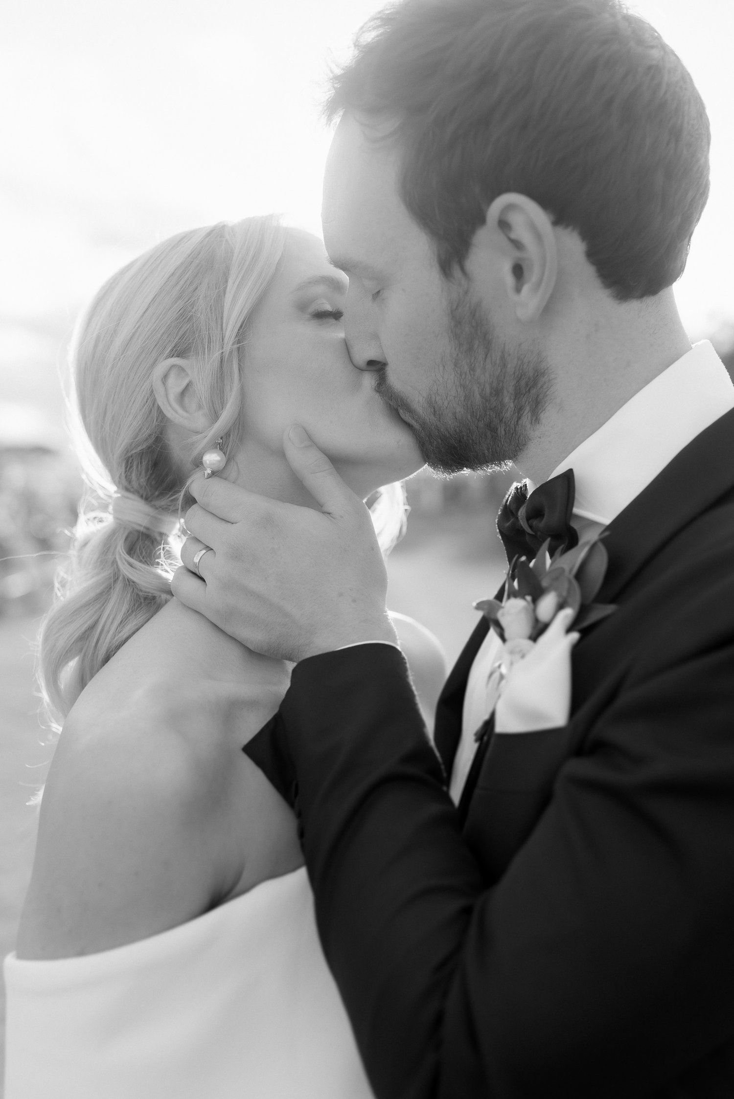 Black and white photo of a couple kissing, the woman wearing a strapless dress and the man in a suit.