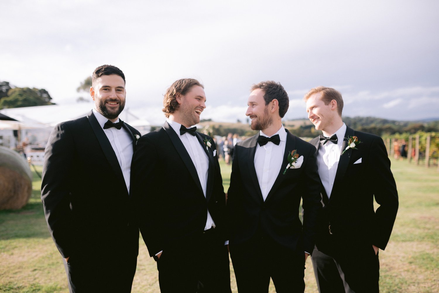 Four men in tuxedos standing outdoors at a wedding.