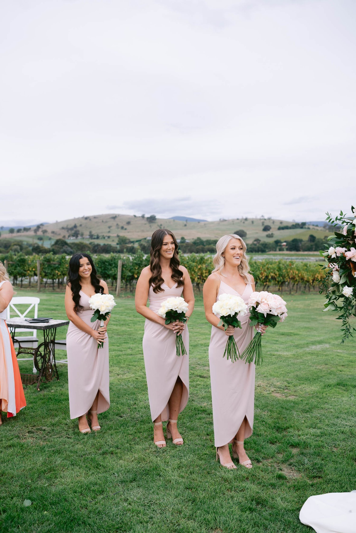 Bridesmaids in blush dresses holding flowers outdoors