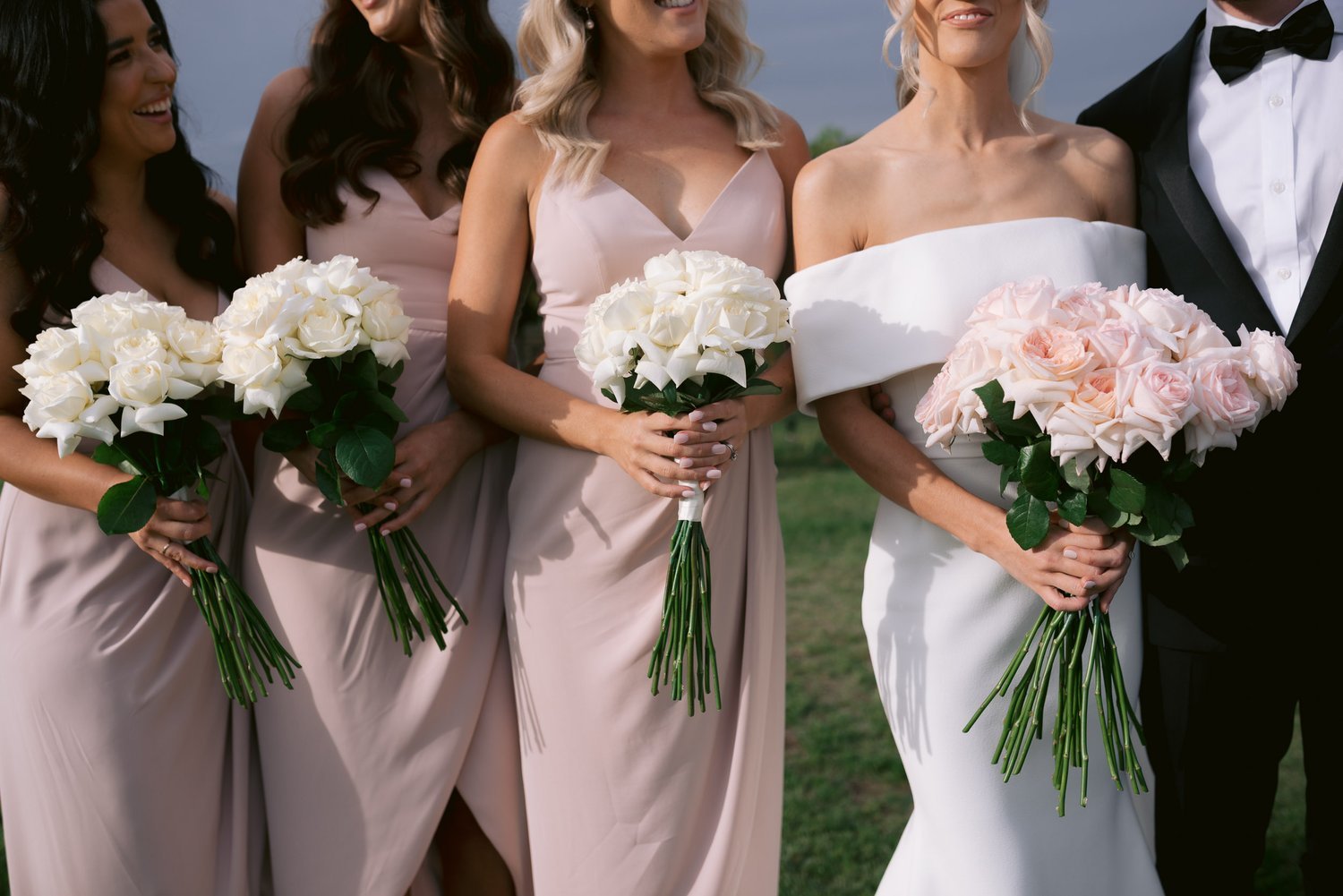 Bridal party with women holding bouquets of roses in light pink dresses.