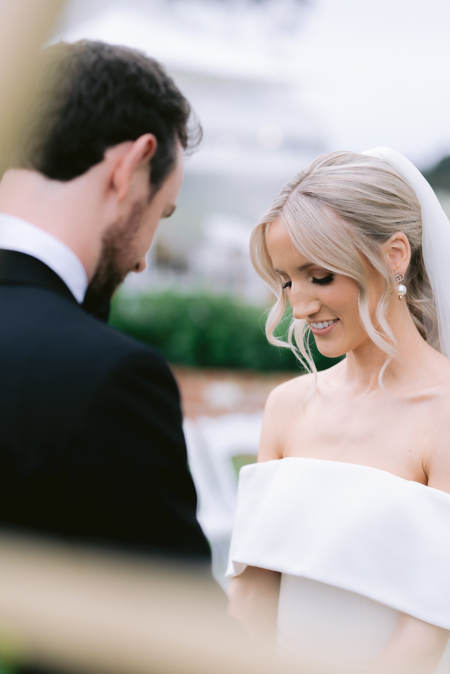 Bride and groom sharing a moment during their wedding ceremony, with the bride wearing an off-shoulder dress and veil.