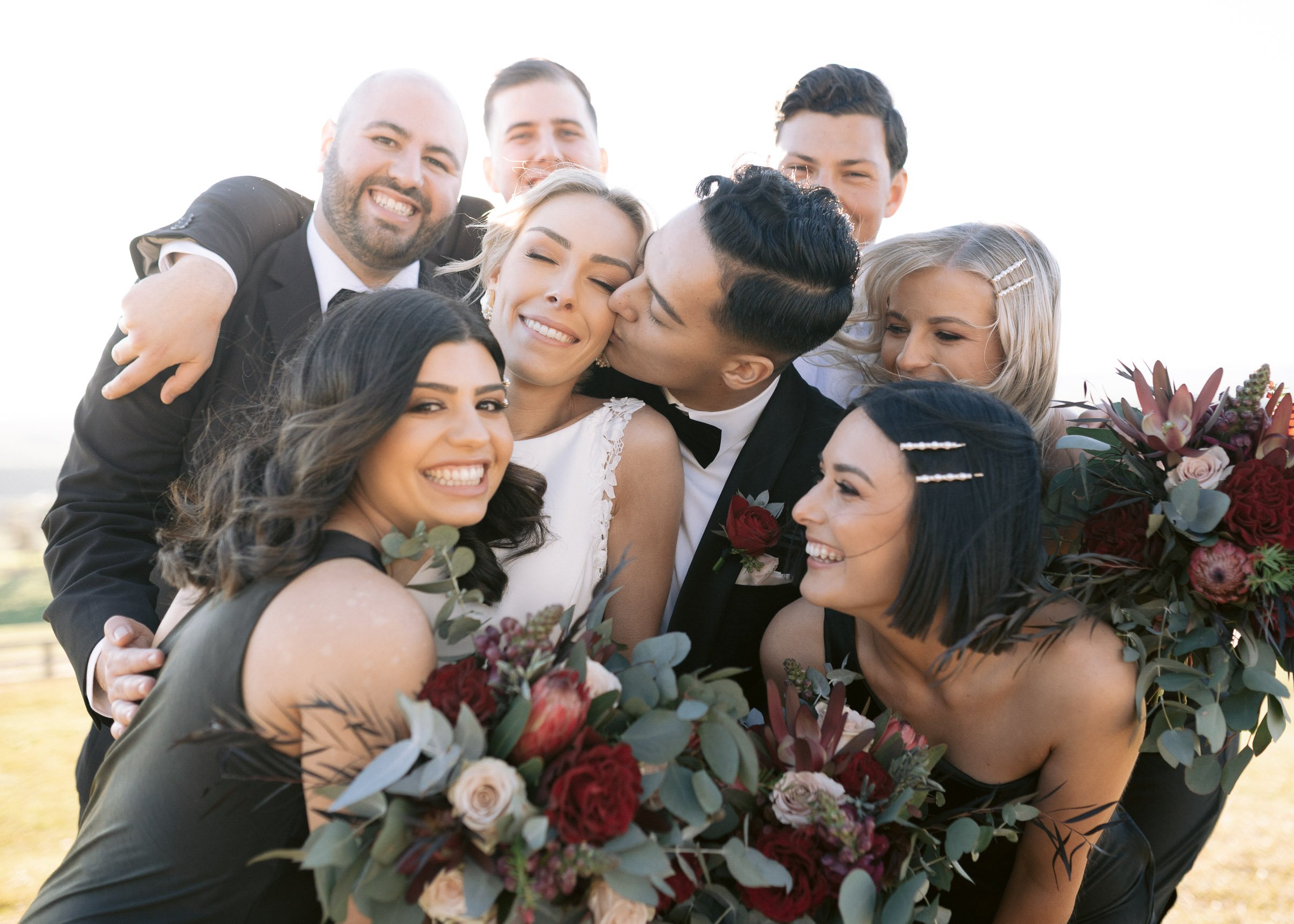Joyful wedding party with bride and groom surrounded by bridesmaids and groomsmen holding bouquets.