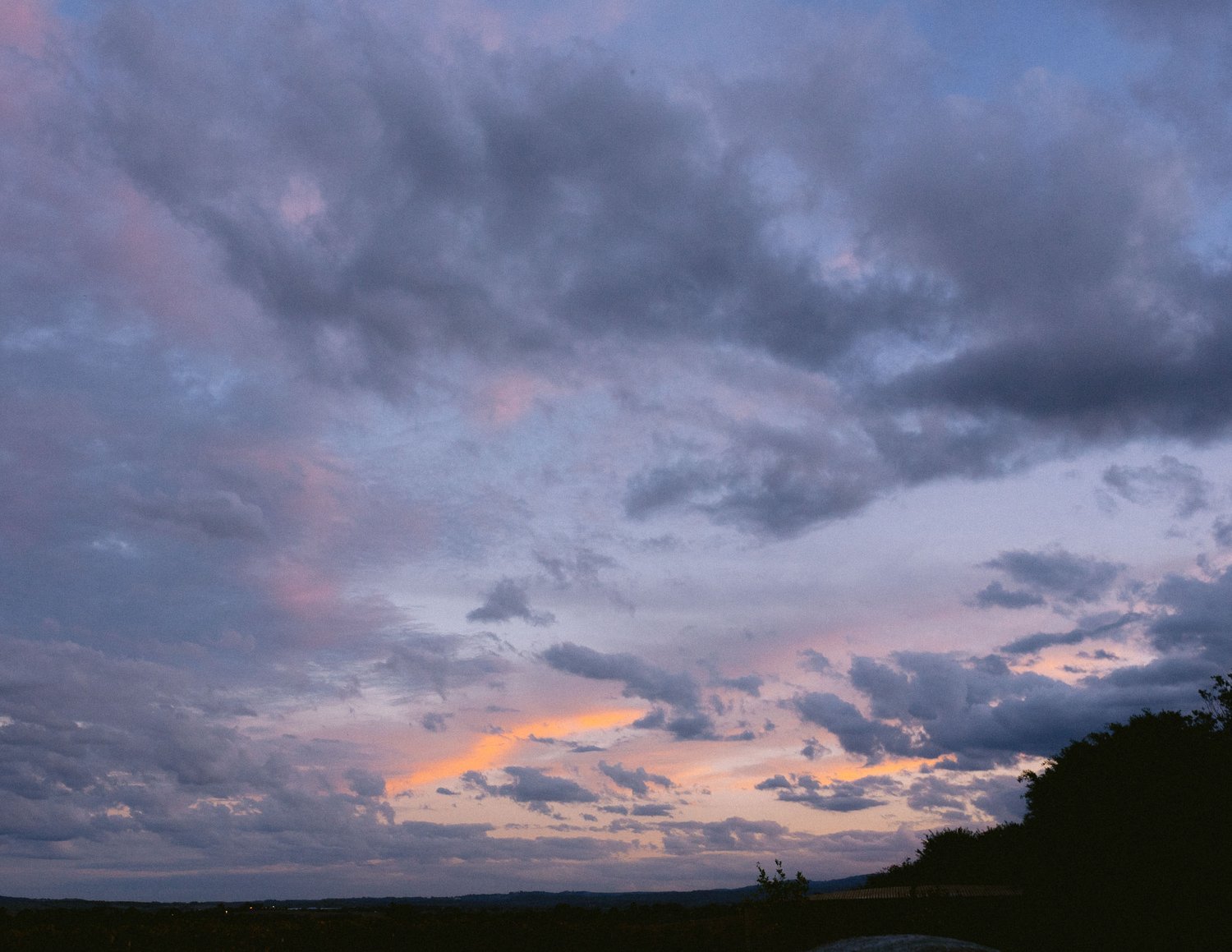 Colorful sunset sky with clouds and silhouette of hills and trees.