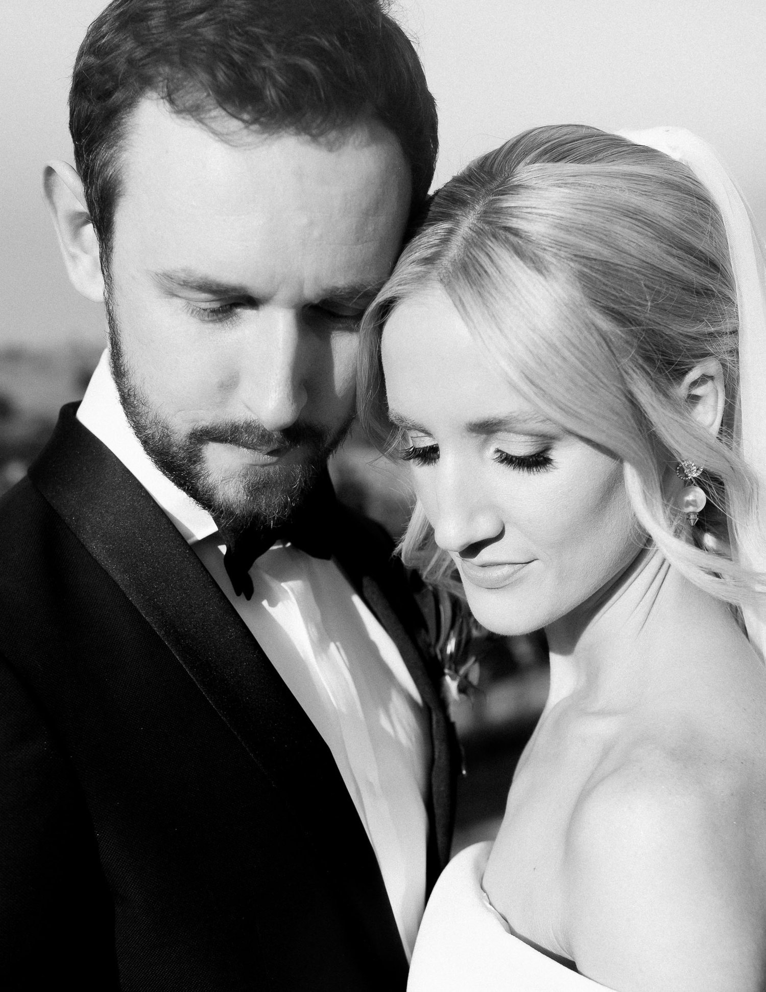 Black and white portrait of a couple embracing, wearing formal wedding attire, with the focus on their peaceful expressions.
