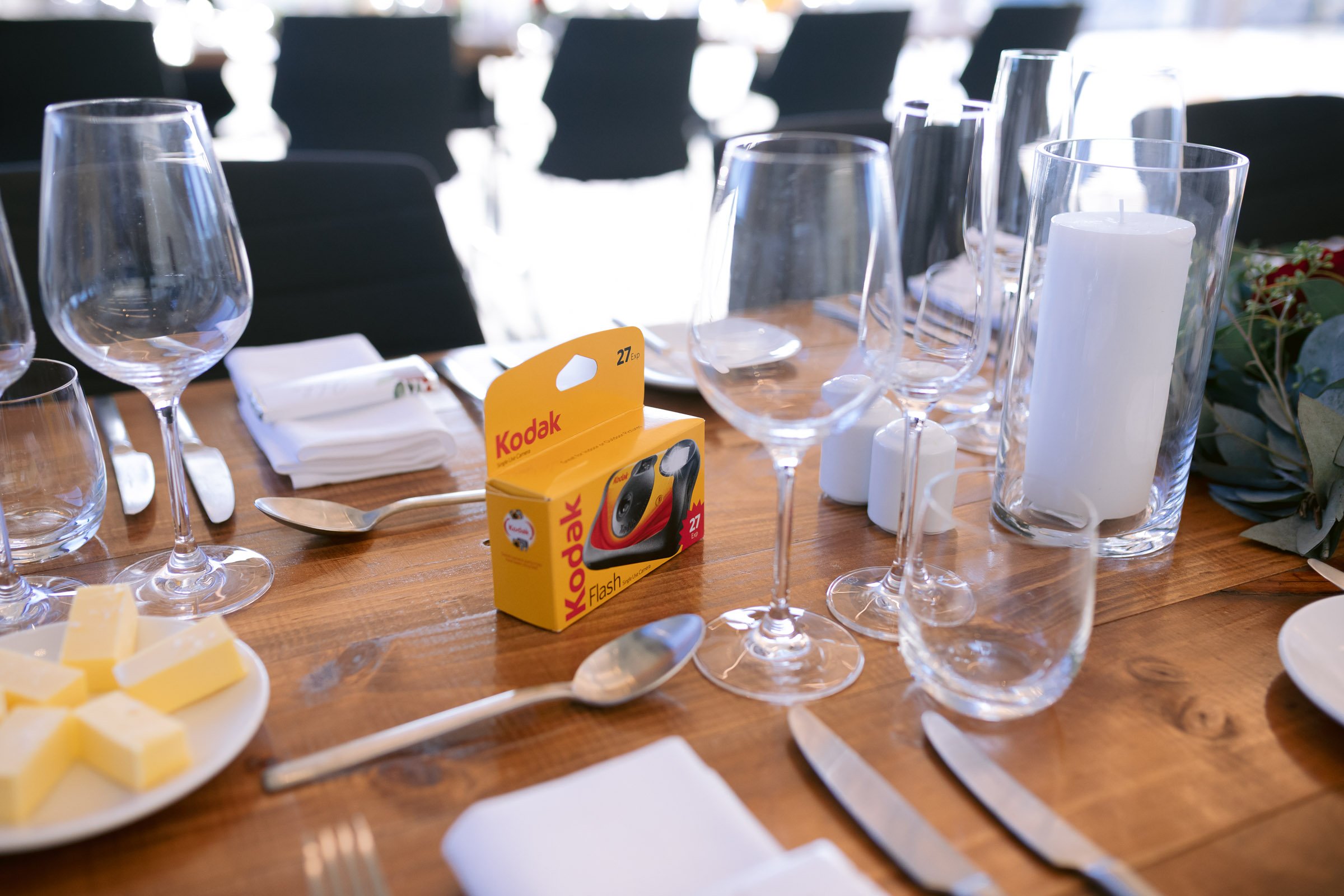 Table setting with wine glasses, a Kodak film box, a candle in a glass holder, and butter on a plate.