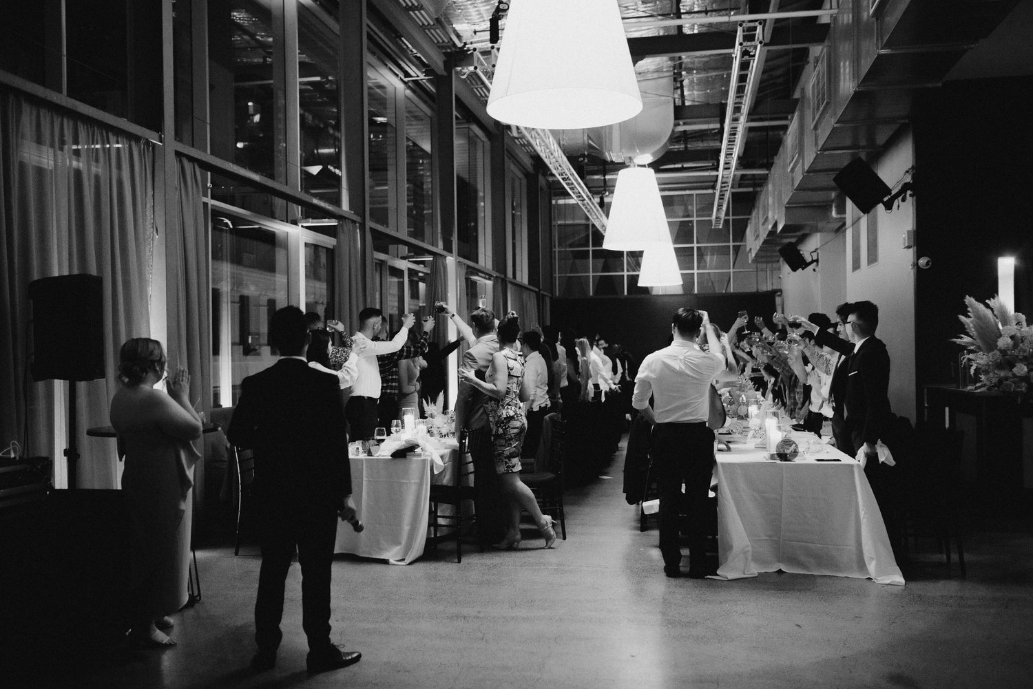 Black and white photo of a formal dinner event with people standing around a long table raising glasses in a toast.