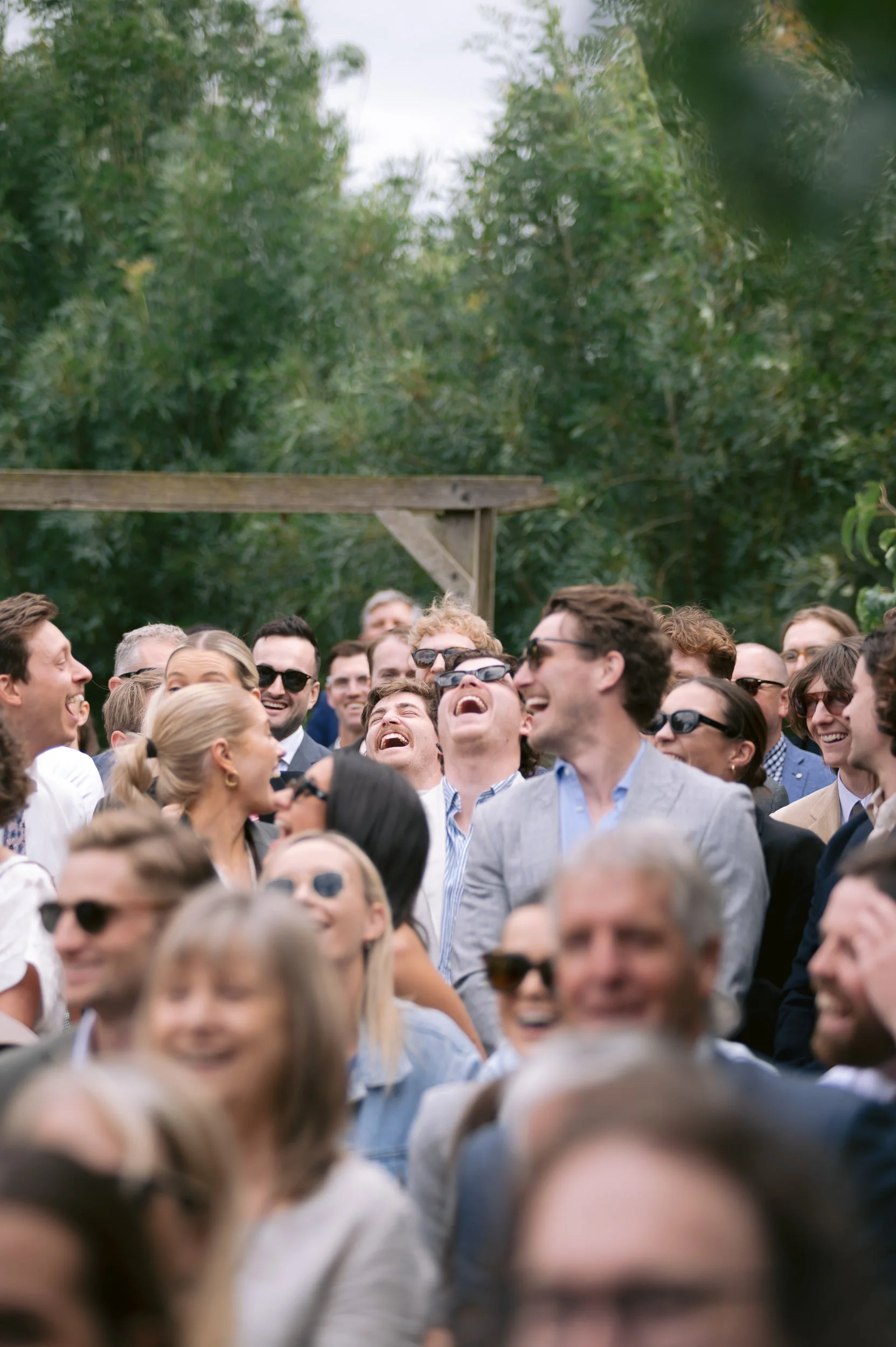 A group of people outdoors, wearing sunglasses and smiling or laughing during a social gathering.