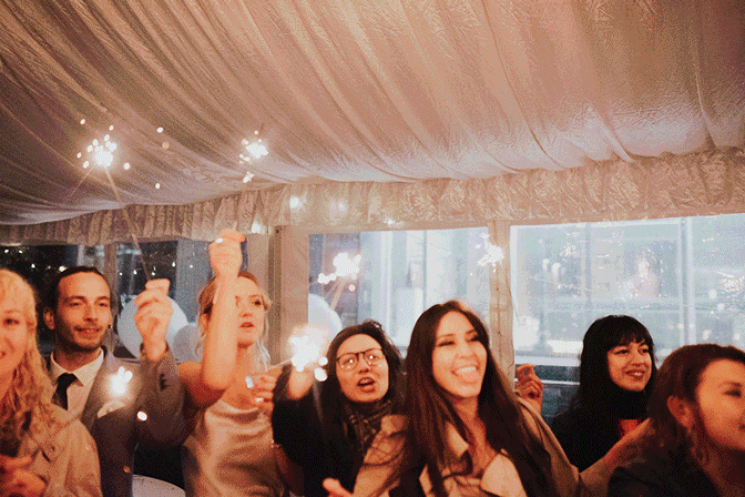 Group of people holding sparklers at an indoor celebration under a white tent.