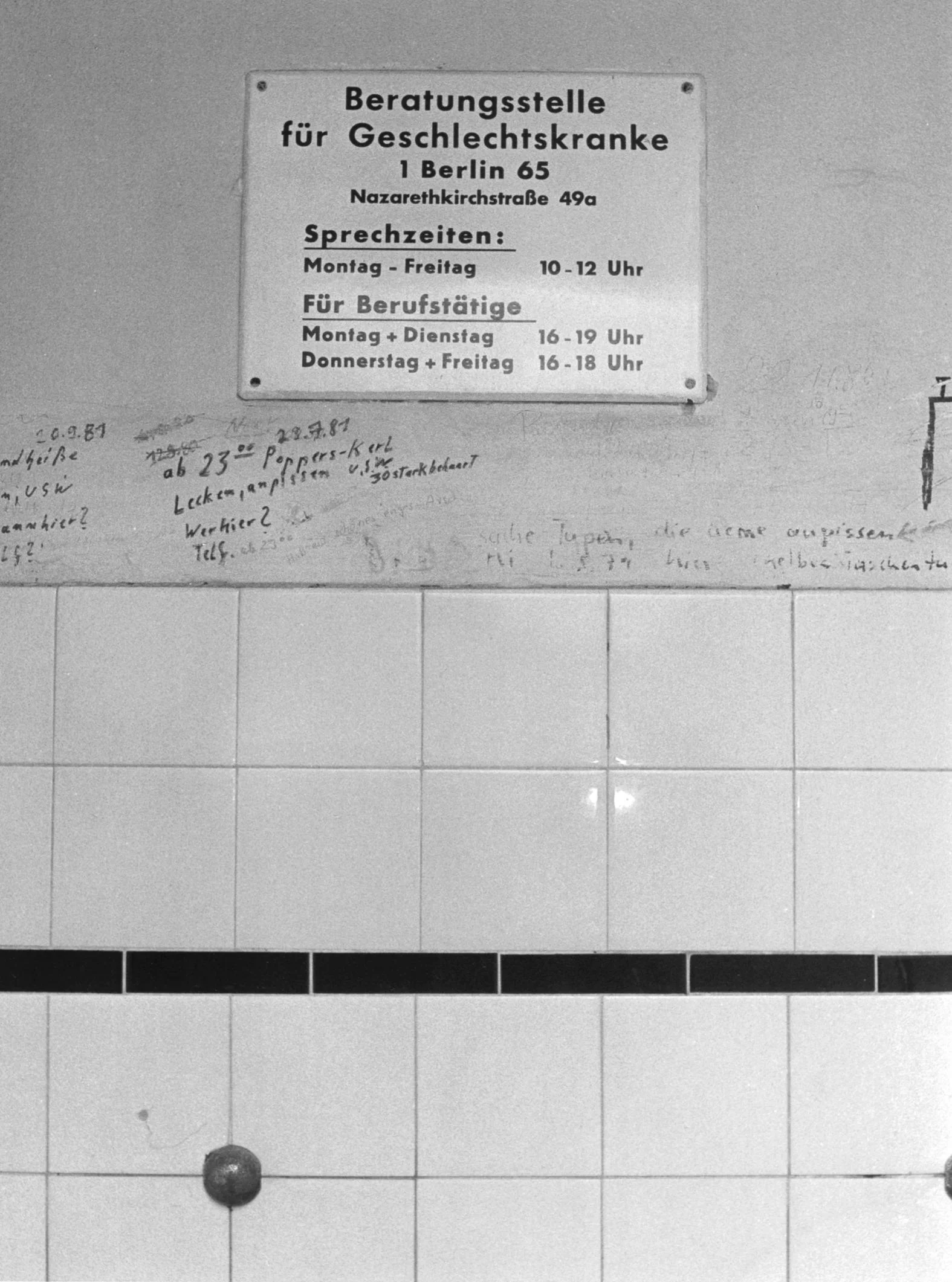 A photo of a West Berlin toilet from 1987 depicts cruising graffiti below a sign directing patrons to a sexual health clinic
