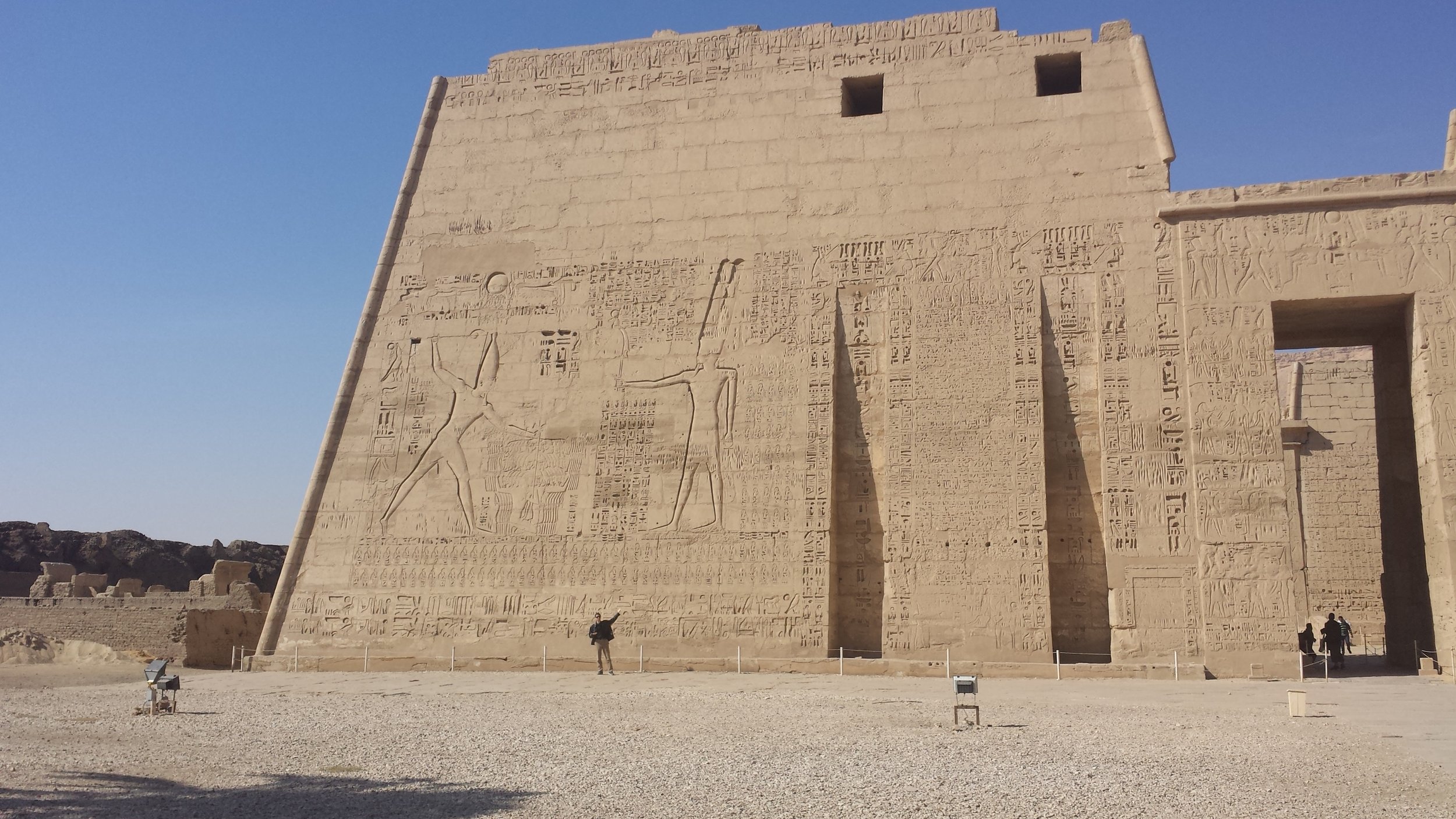 The entry pylon to Habu temple. Some fool is standing in front of it to give a sense of scale. It depicts Ramses III making offering to Ra.