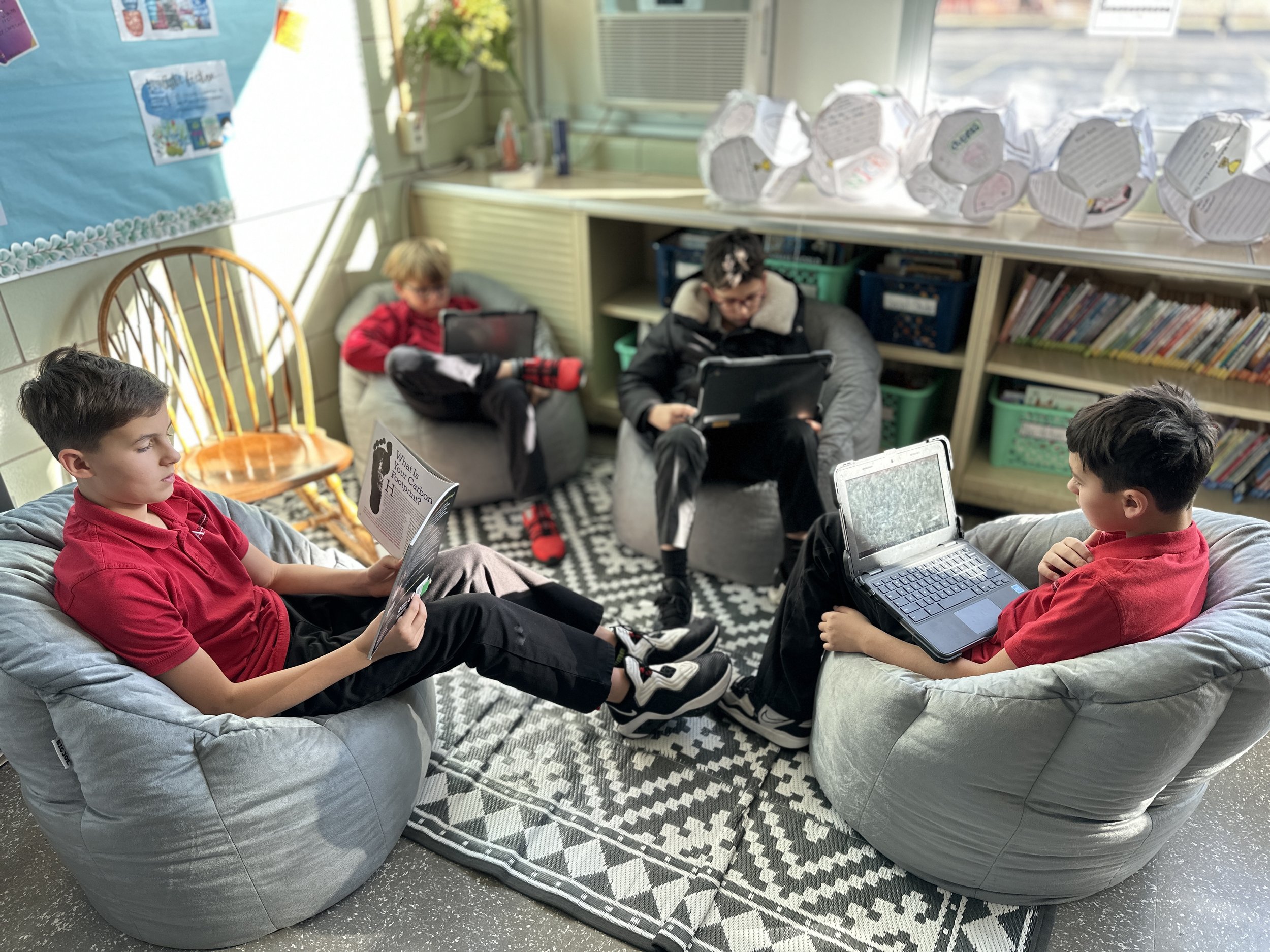  Four fifth grade boys are collaborating in the back corner while sitting on bean bag chairs 