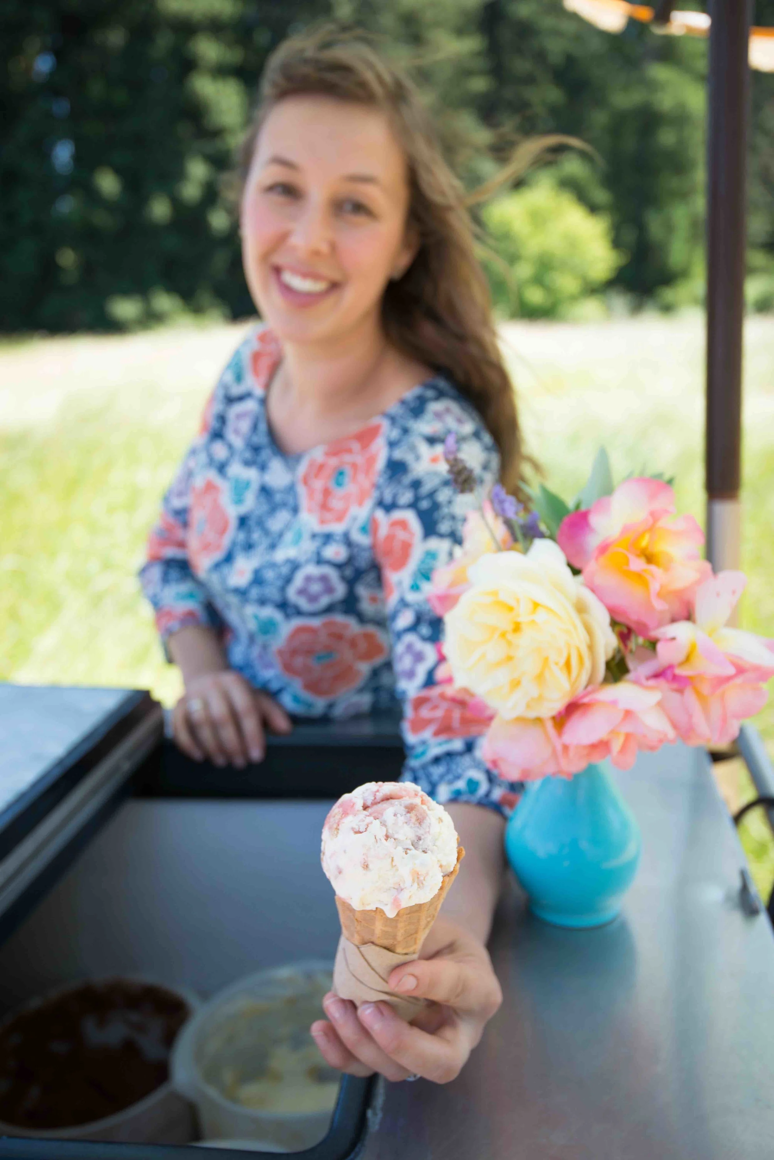 person in a flowered dress serving ice cream cone out of a mobile ice cream cart.jpg