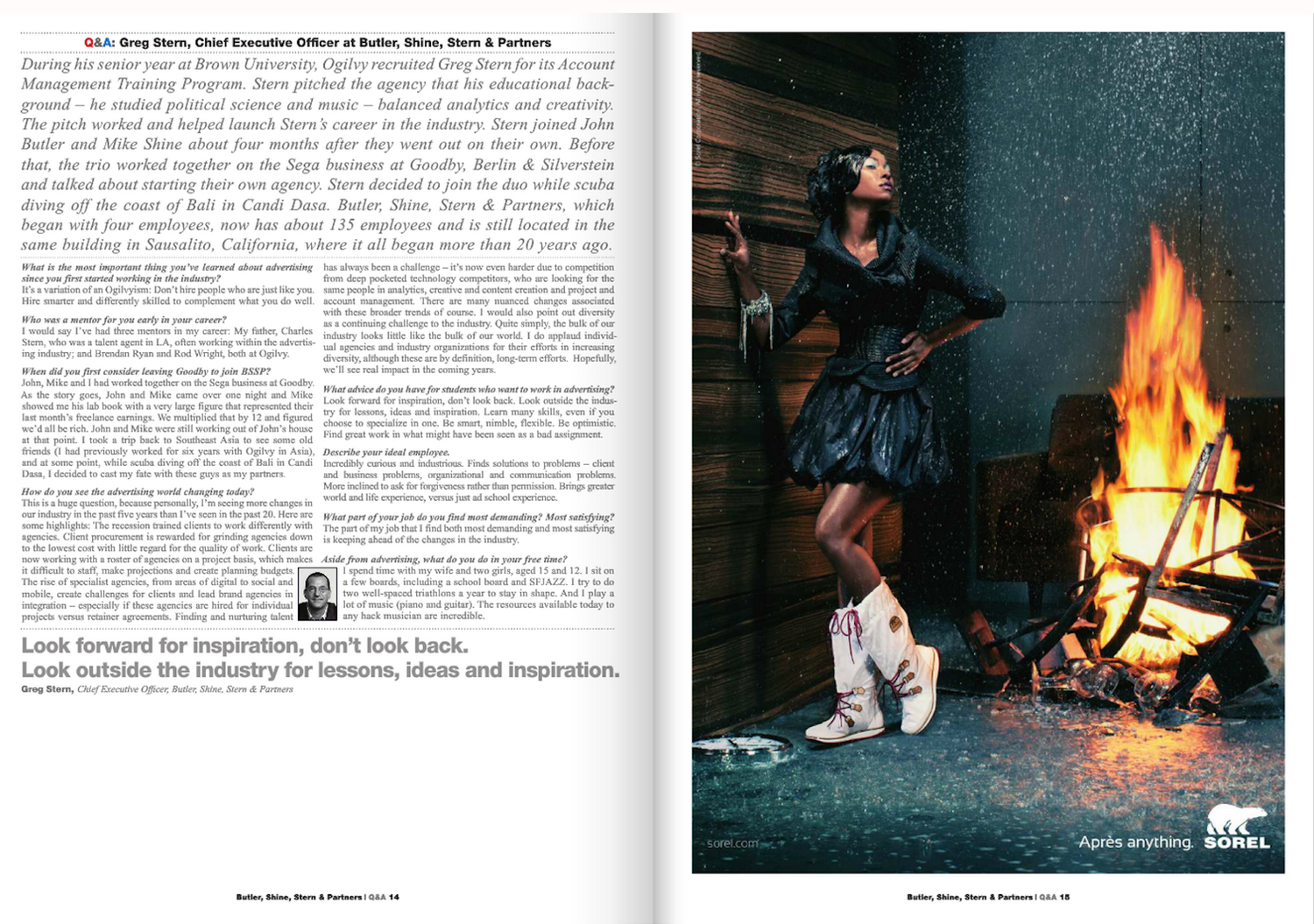 A woman standing next to a fire in a smoky outdoor setting at night, wearing a dark, waterproof jacket, a matching skirt, and lace-up boots, with her hand on her hip and her head tilted back, looking away from the fire.