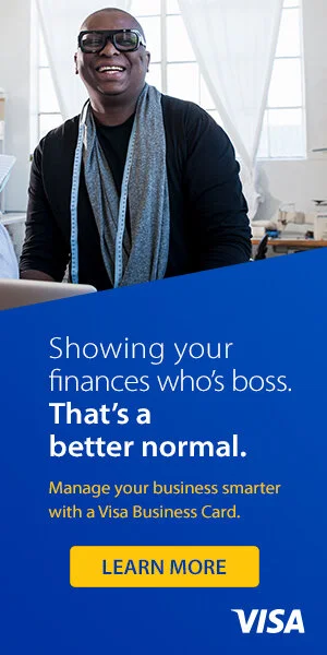 Visa digital banner of smiling woman wearing glasses and a scarf, sitting at a desk in an office with large windows and white curtains.