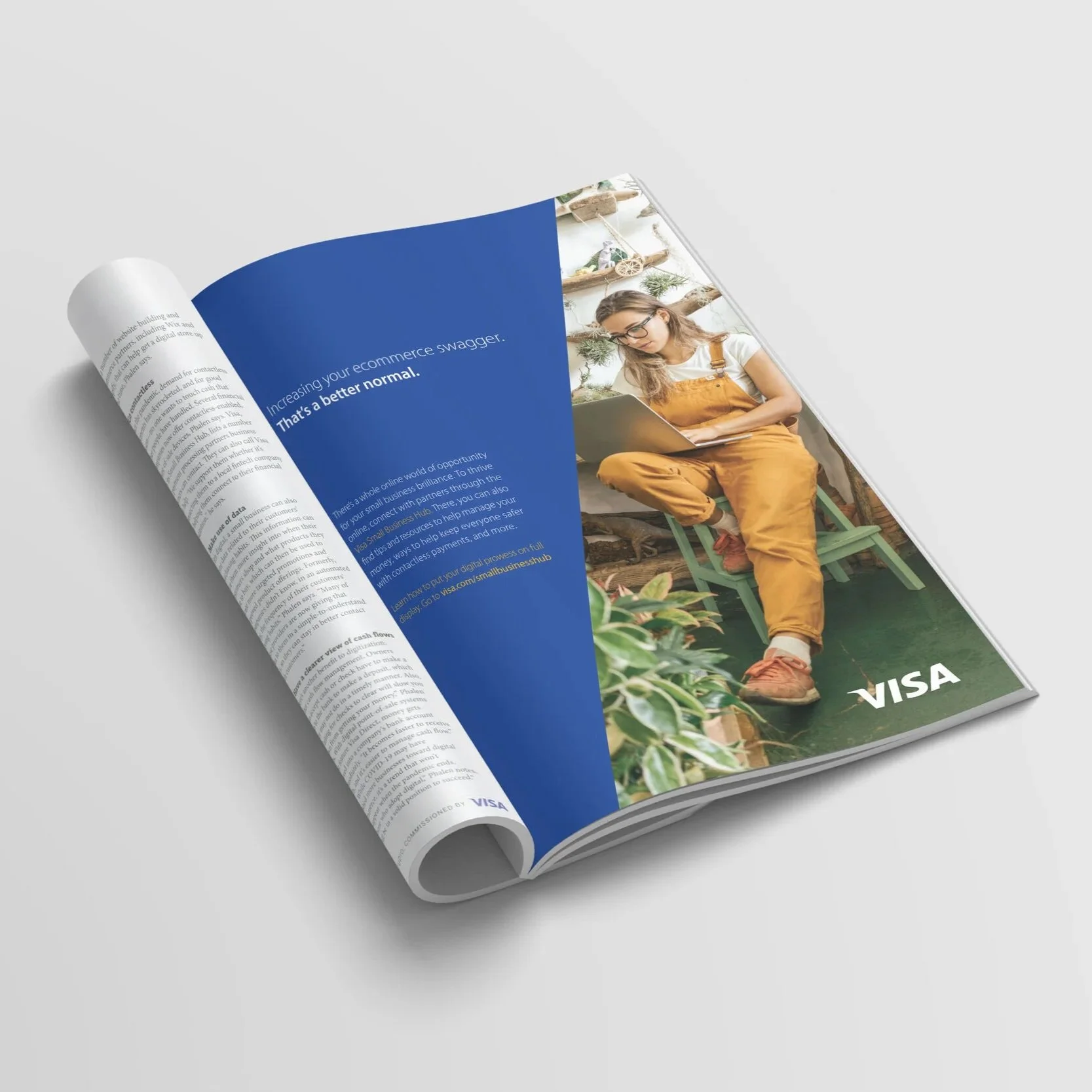 An open magazine featuring a colorful advertisement for Visa, displaying a woman wearing glasses, sitting in a wooden chair, using a laptop, with decorative plants and shelves in the background.