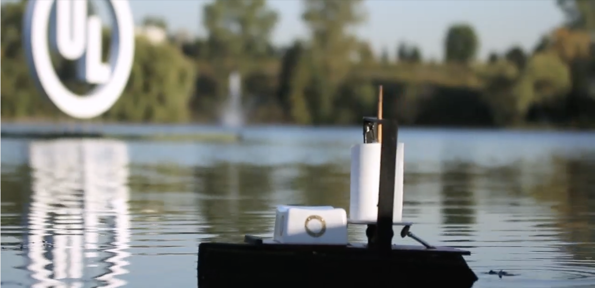 Close-up of wind powered boat created by Robert L Sylvester for the UL Solutions Winderrific video cruising in a pond with lush green trees and blue sky in the background.