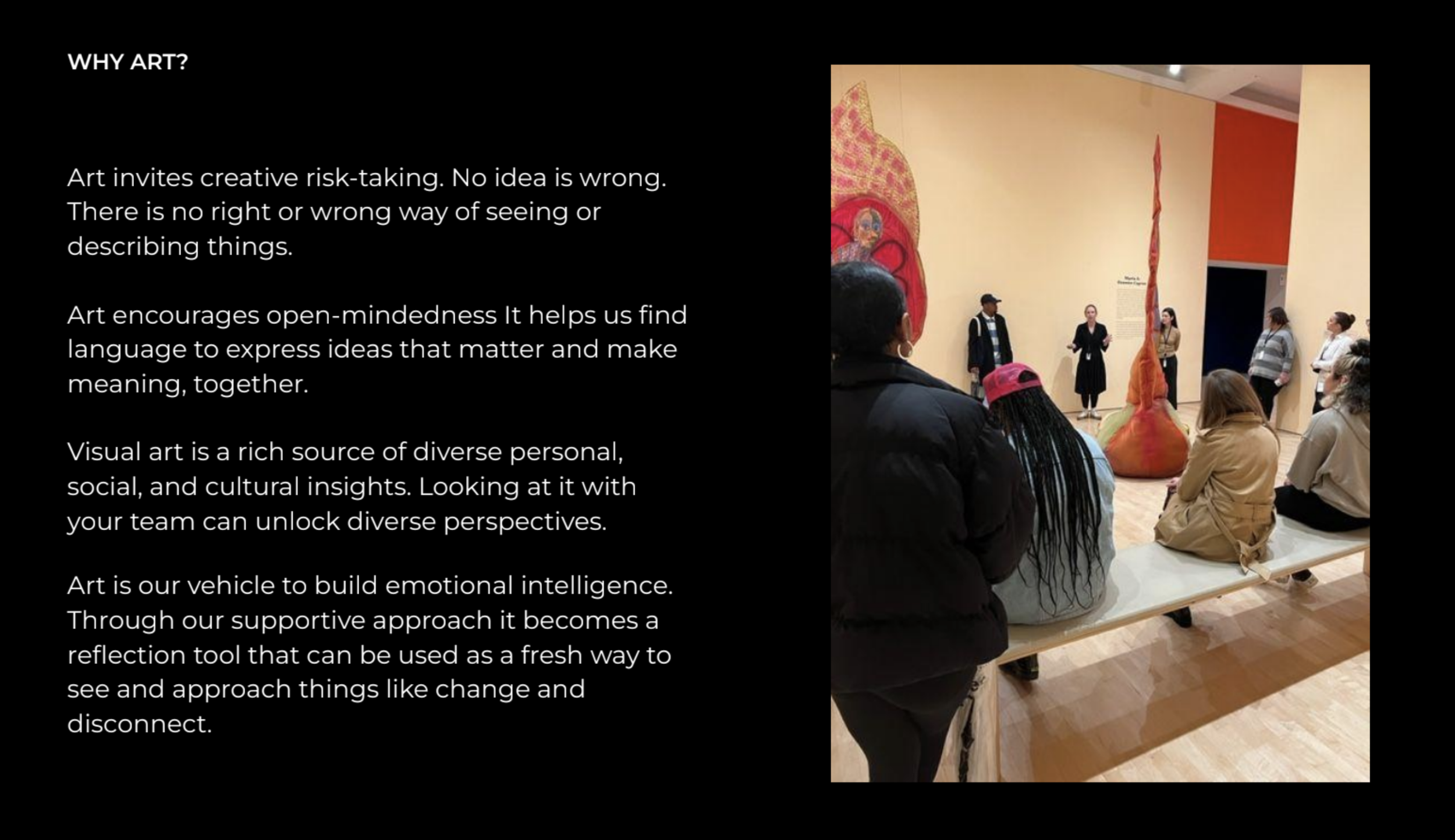 A group of people are sitting on a bench and standing in front of an art installation in a gallery, with colorful wall paintings and a beige wall.