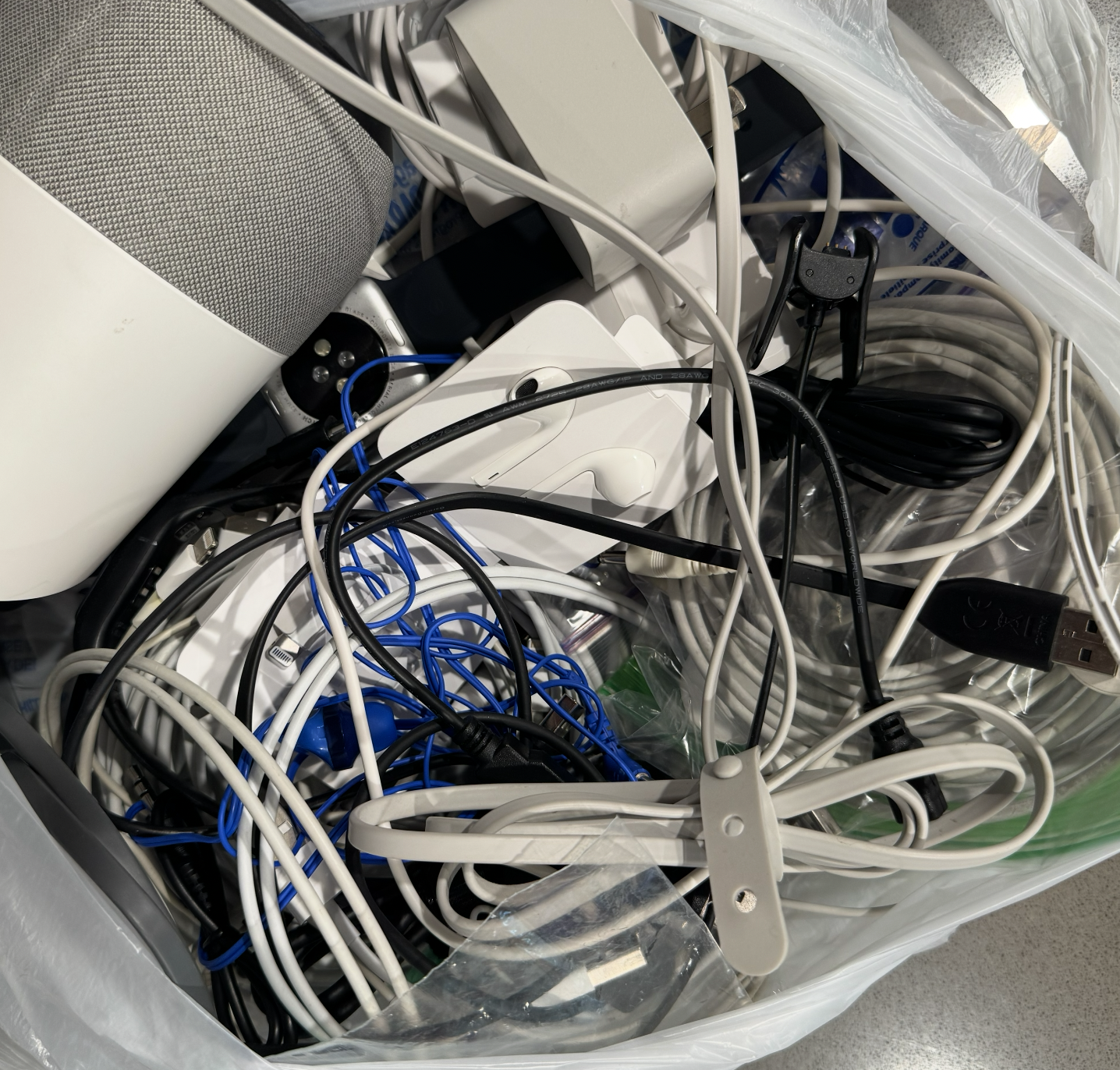 A pile of tangled electronic cords, plugs, and adapters in a plastic bag.