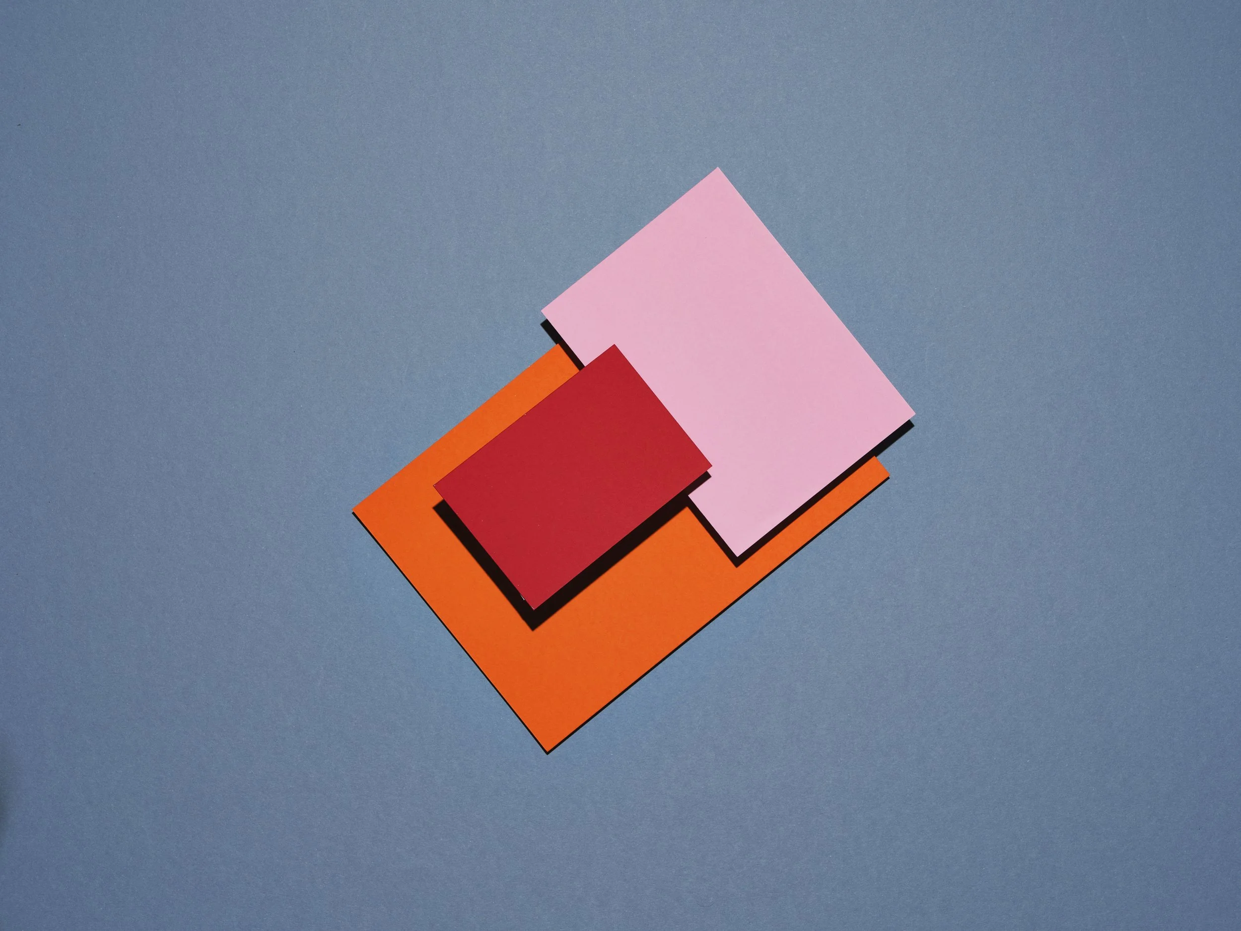 Coloured pieces of cardboard on a blue background. Abstract image of a mood. Pink, Red and orange rectangles.
