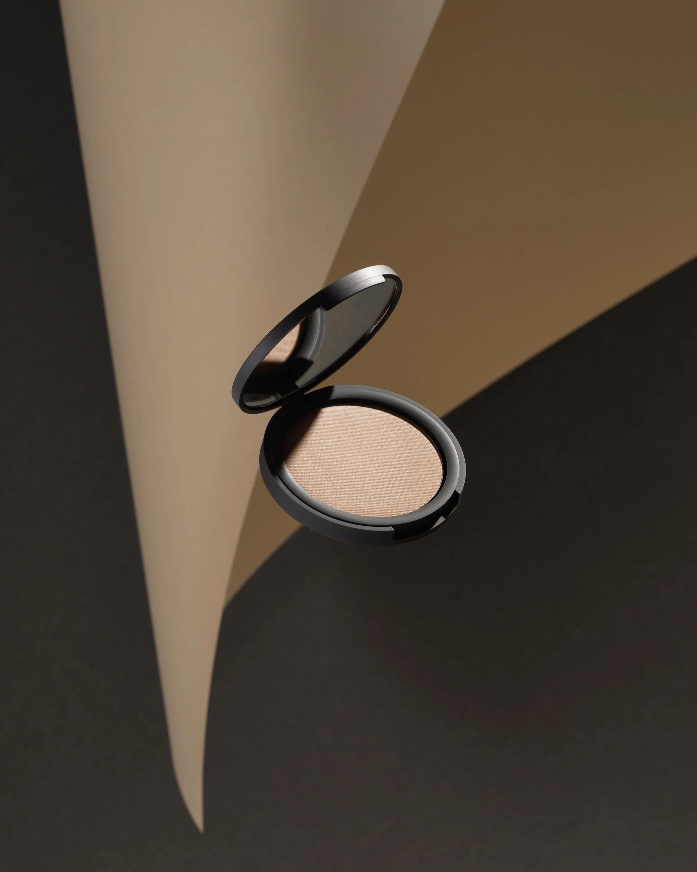 Floating piece of make-up on an abstract piece of paper on a dark grey back ground.