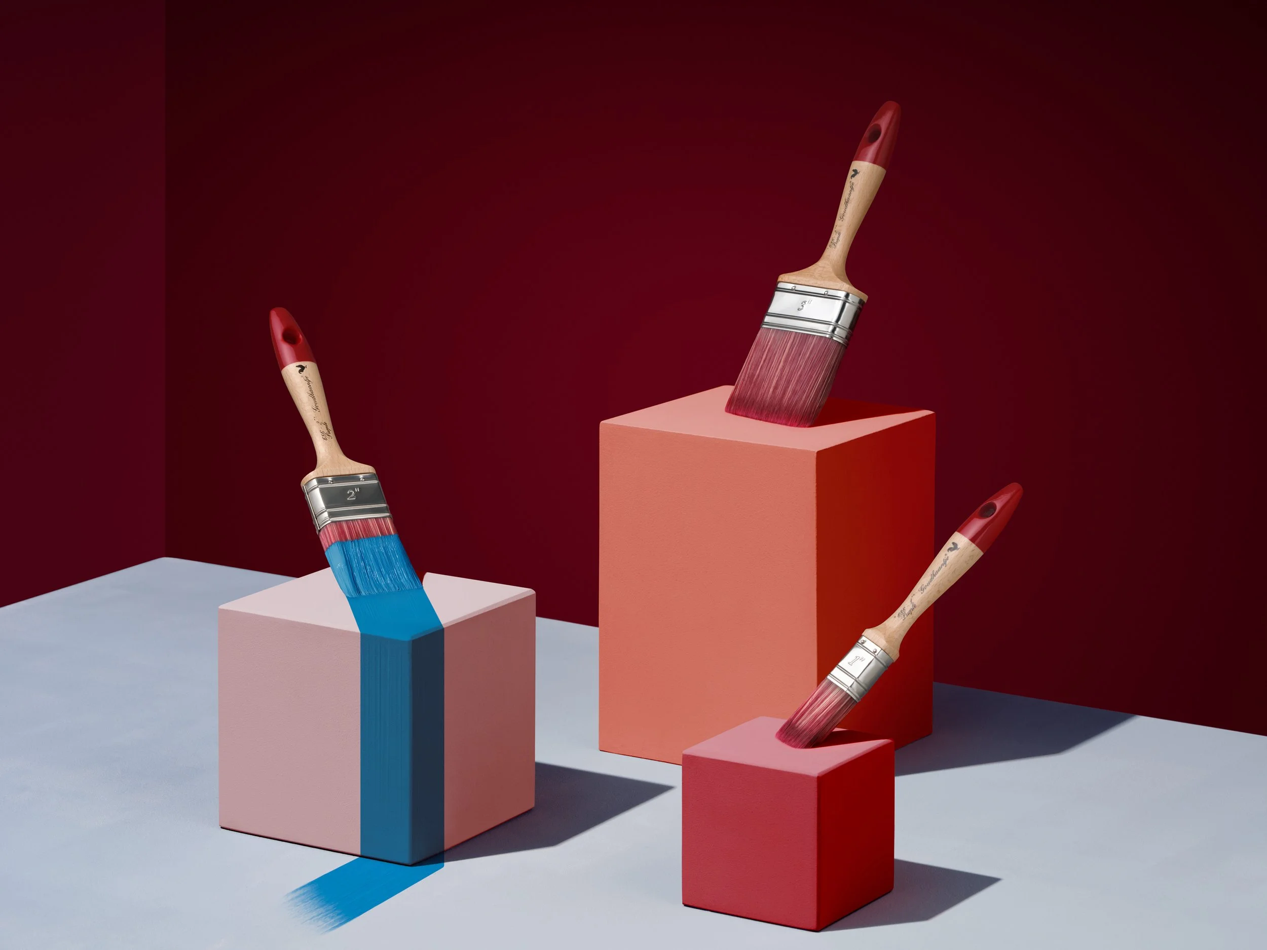 Paintbrushes with red and blue paint are placed on pastel-colored cubes against a dark red background.