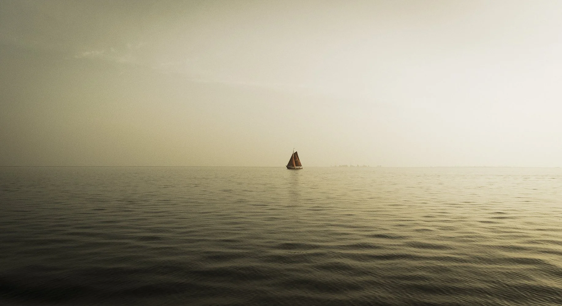 A sailing ship photographed on a empty lake, with a red sail, autumn light