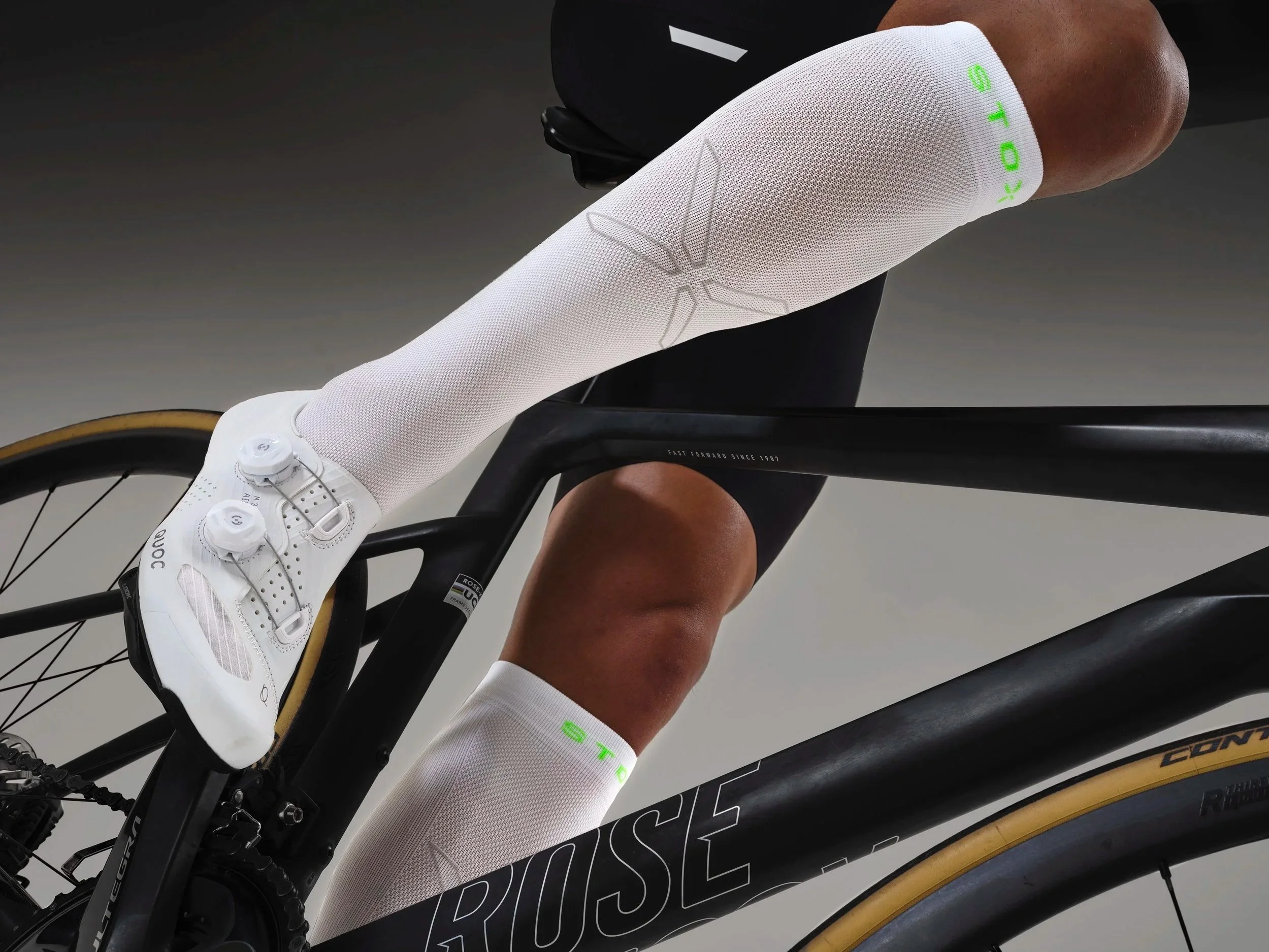 studio shot of a cyclist wearing white Stox energy socks from their cycling range,  shot from a low angle on a black bike