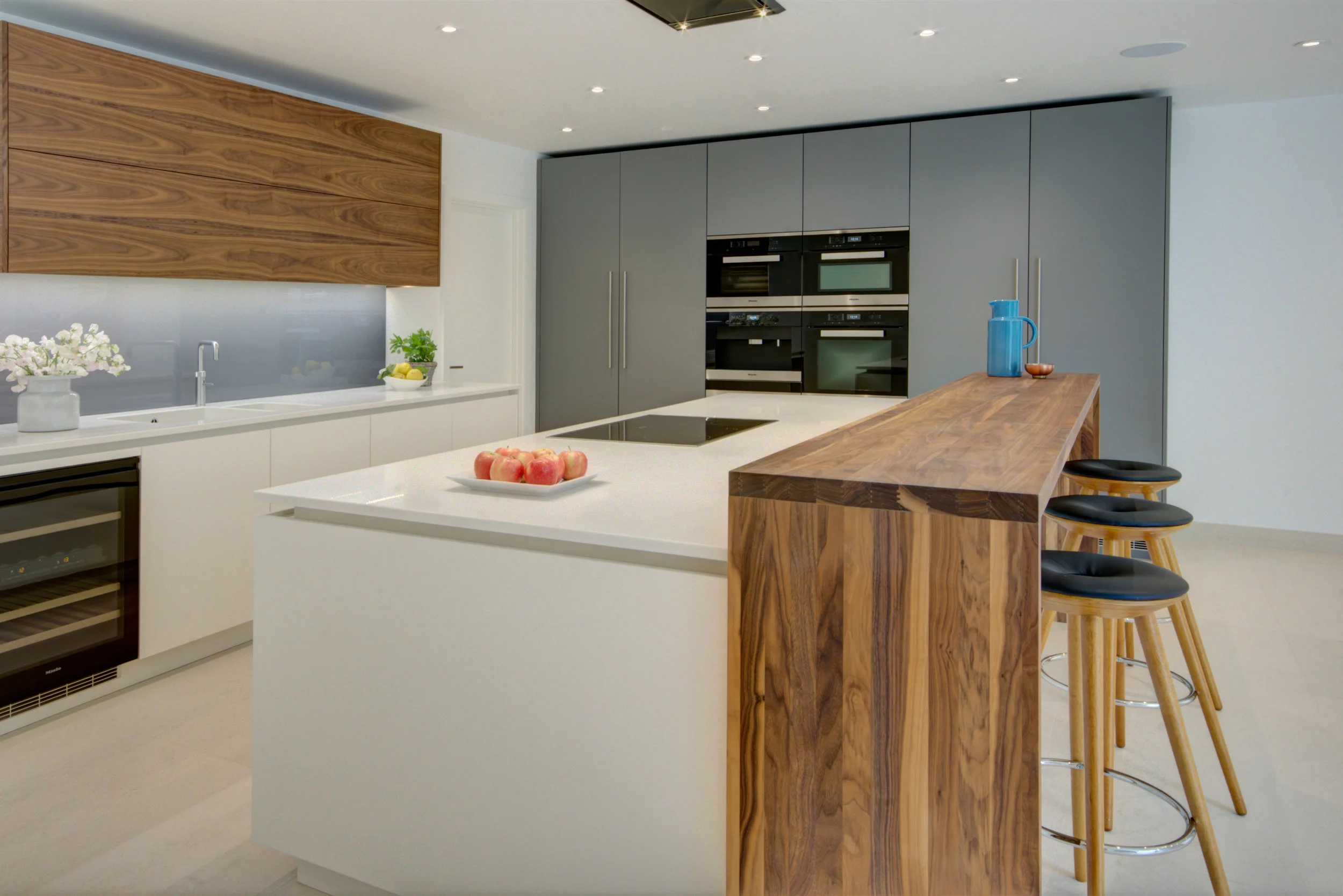 Contemporary kitchen design for a modern development with light coloured painted base units, walnut wall units and bar.