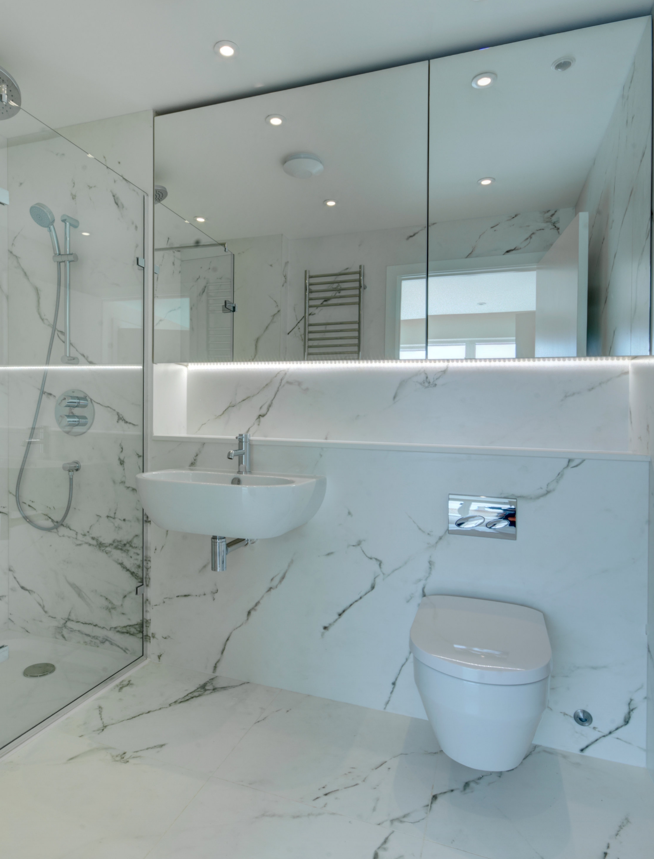 Bathroom design with marble effect wall finish and bespoke mirror cabinet.
