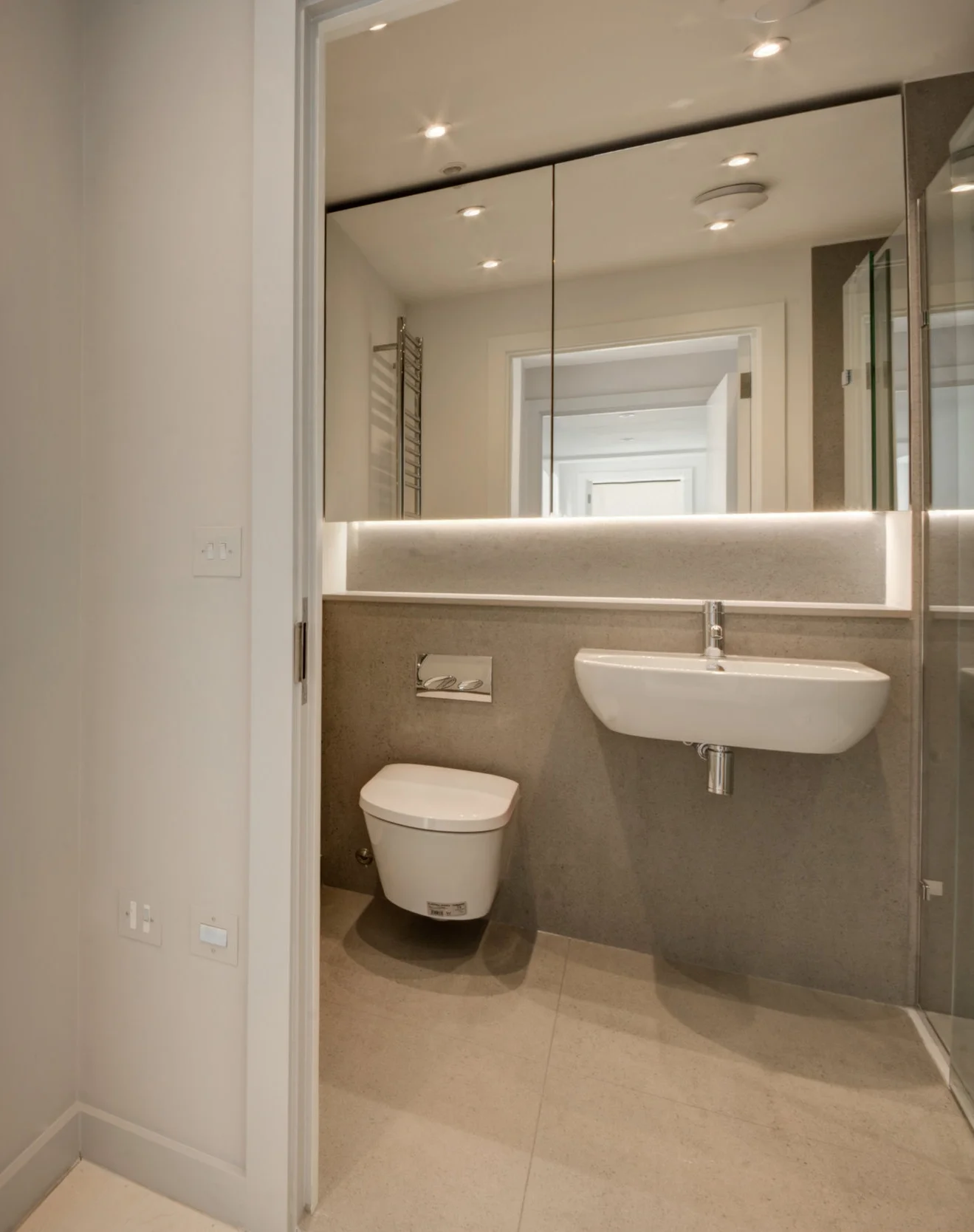 Bathroom design with white WC and basic with grey stone wall cladding and tiles and bespoke mirror cabinet.
