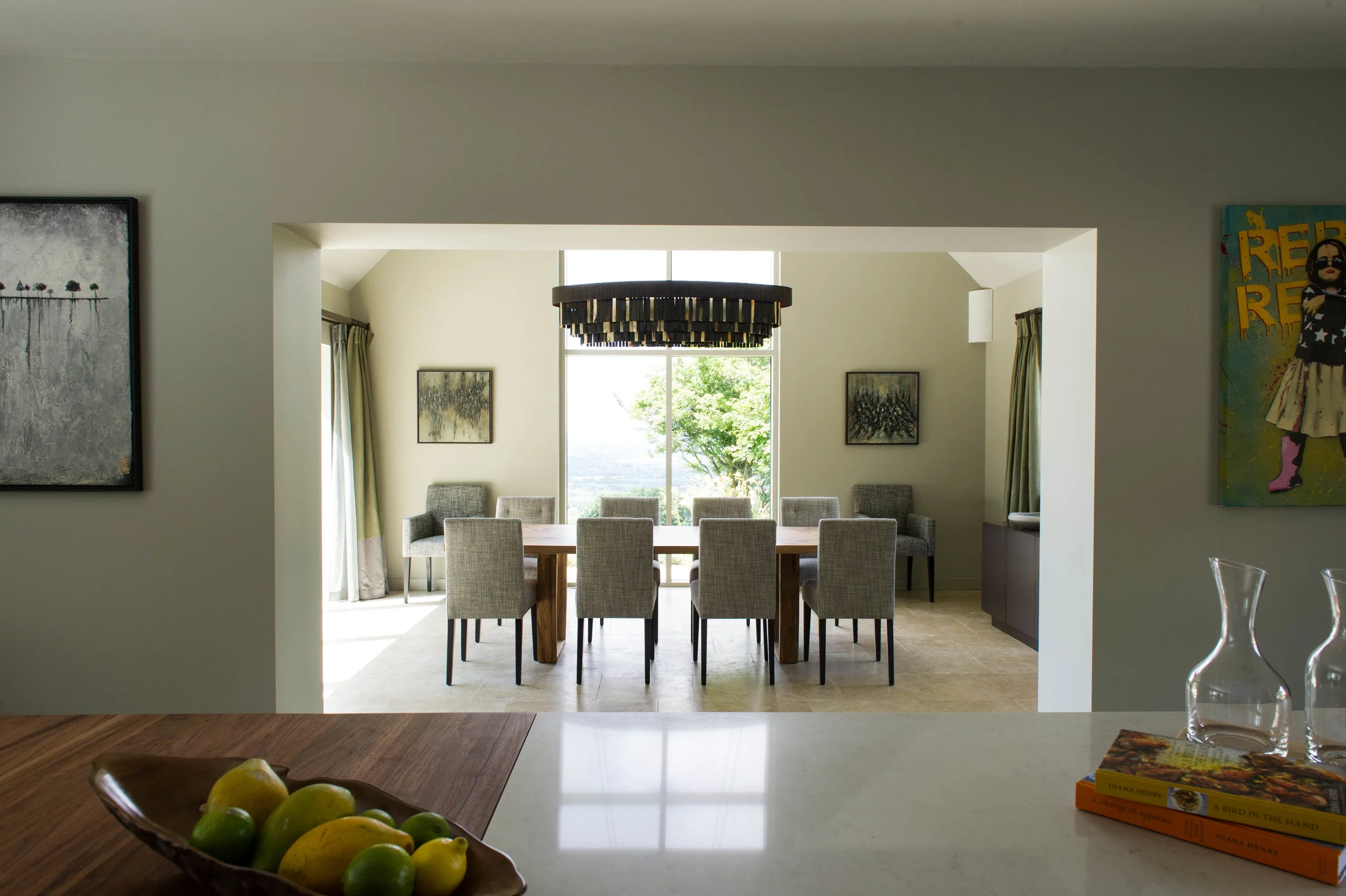 View into dining room from kitchen island unit. Timber dining table with grey upholstered chairs and contemporary chandelier. By Joseph Interior Design, Cheltenham.