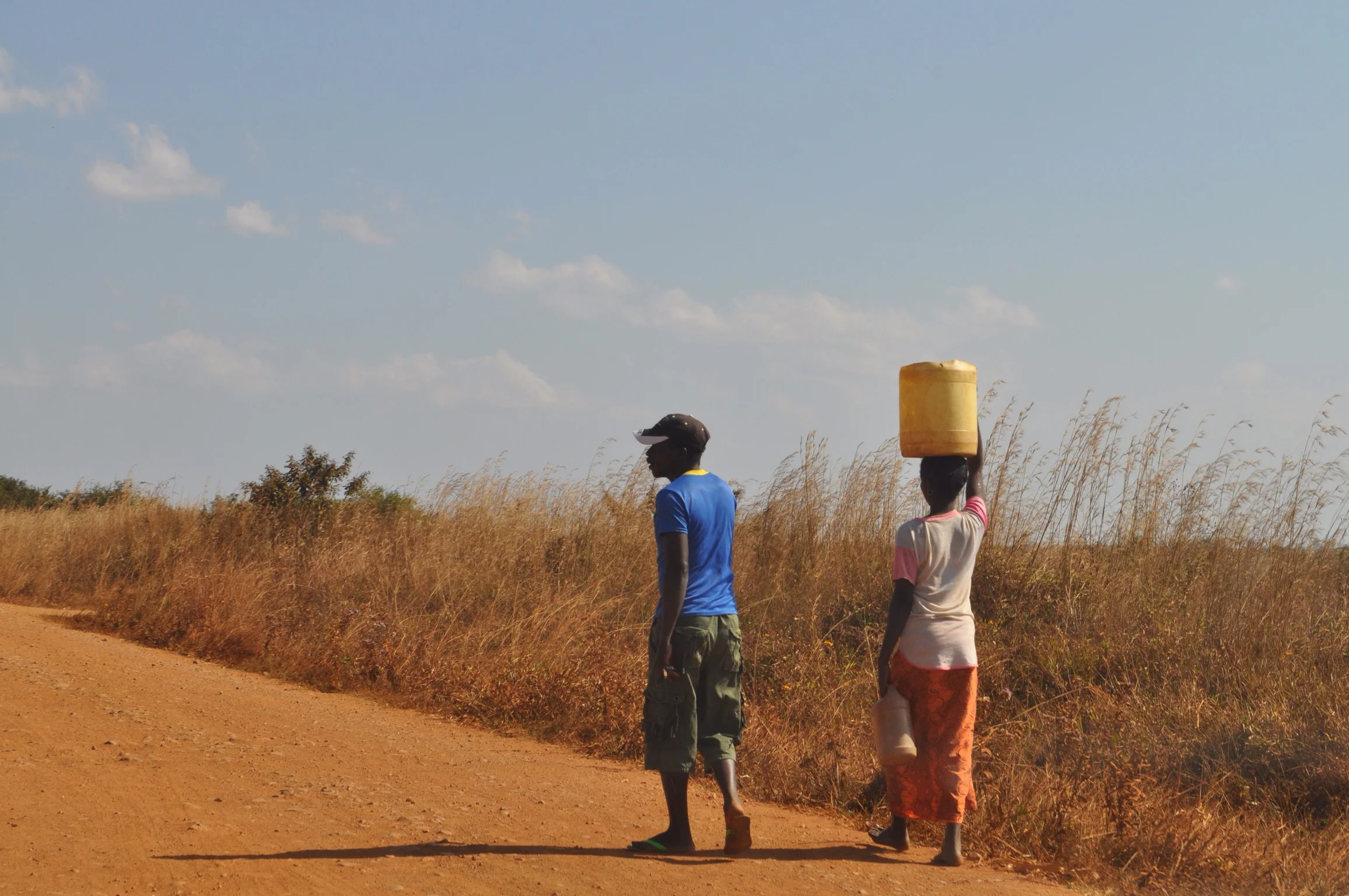 A common sight on the road... Woman carrying multiple jugs of water while the man carries nothing...