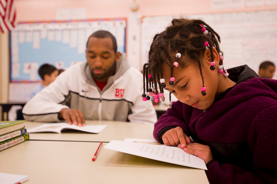  BU basketball team member Travis Robinson (SMG'14), left, follows along with Ilanddy Peres while she reads "Owl at Home" during the basketball team's recent visit to Sterling Scott's second grade classroom at Blackstone Elementary on December 13, 20