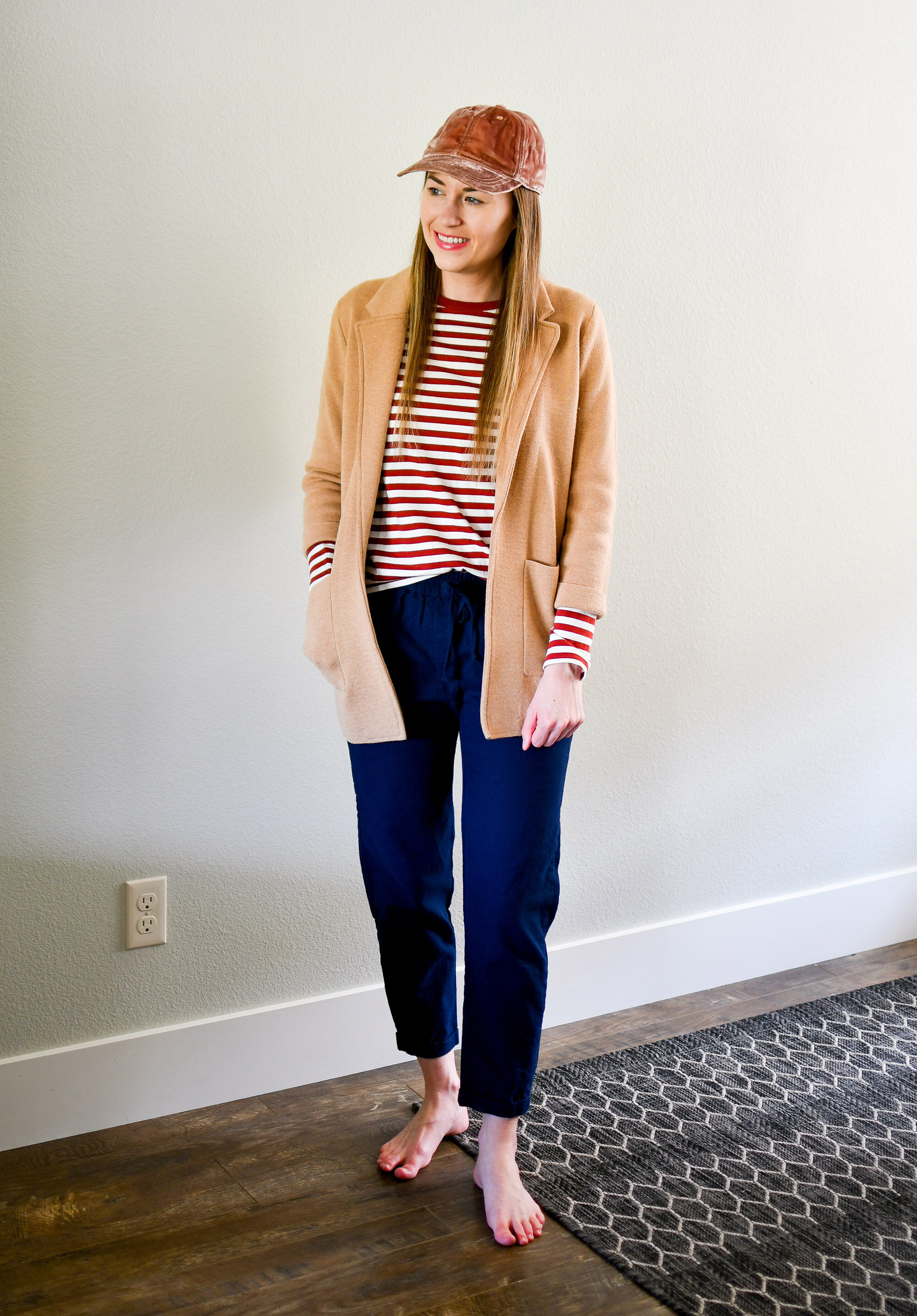 Spring work from home outfit with camel sweater blazer, red striped tee, navy pants, pink baseball cap — Cotton Cashmere Cat Hair